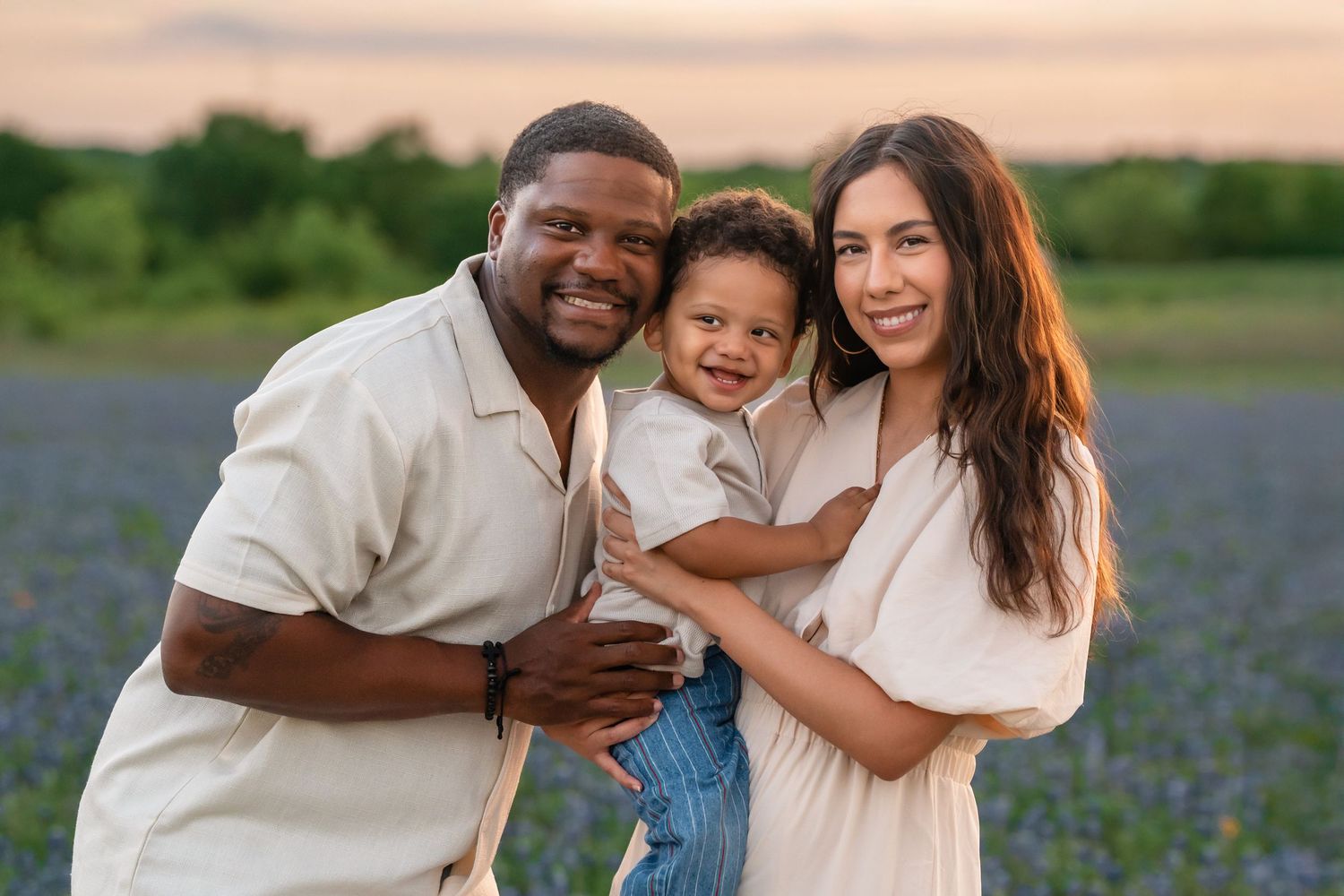 A family shares joyful moments together while taking outdoor photos in a field of bluebonnets at sunset.