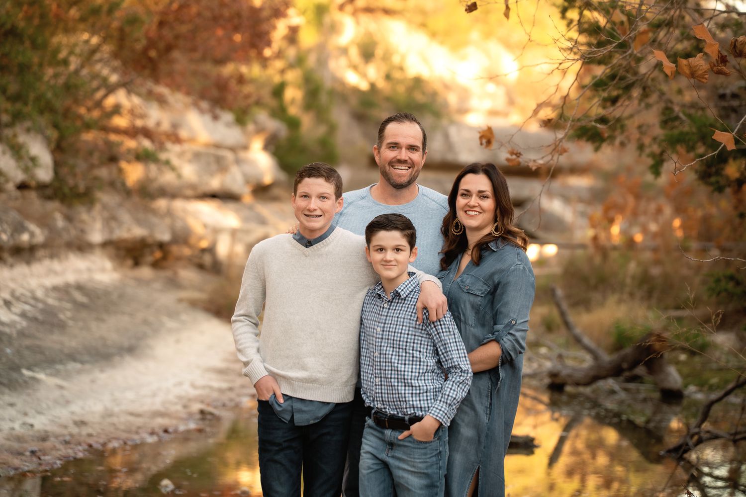 A group poses for outdoor family portraits in a natural setting during golden hour with autumn foliage.
