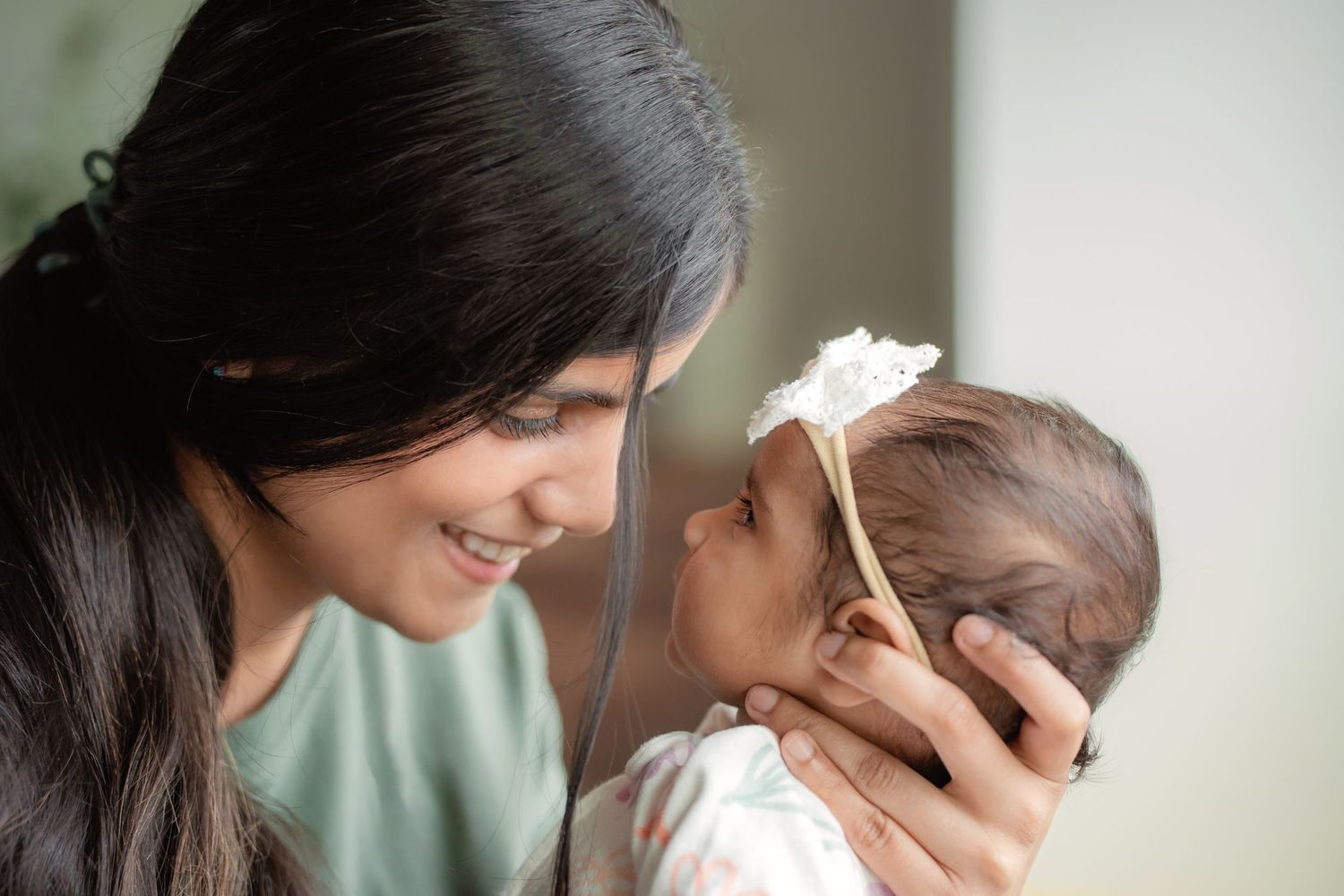 A smiling mother tenderly holds her newborn baby close, sharing a gentle moment of bonding.