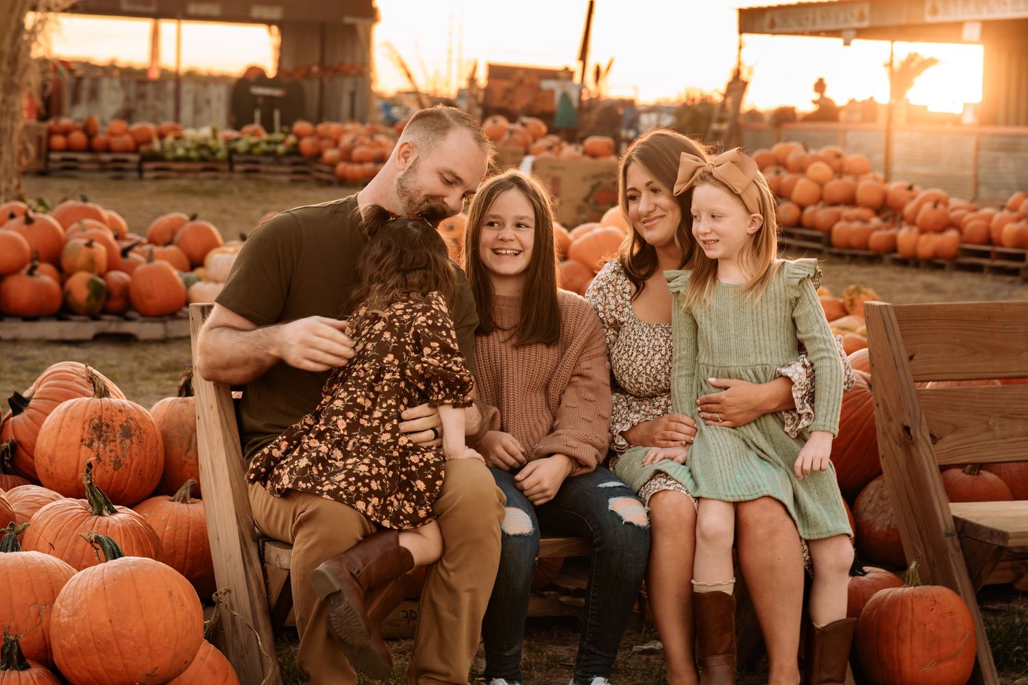 Five family members in a warm autumn scene at Mama Mary's Pumpkin Patch during sunset with orange pumpkins and cozy gatherings.