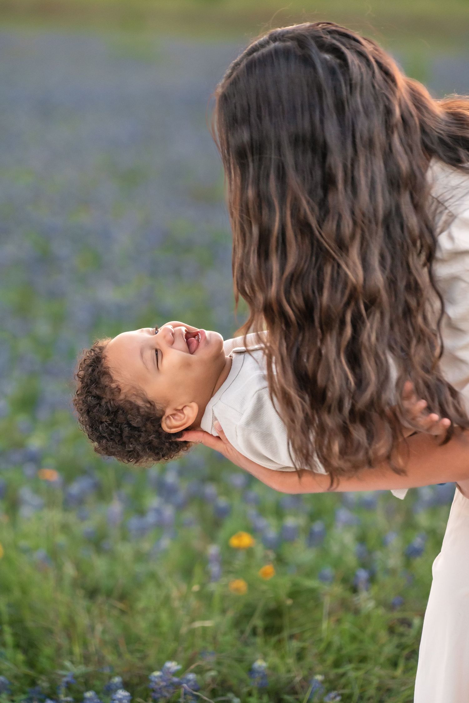 A joyful moment captured in a field of wildflowers as a parent lifts a laughing child wearing white.
