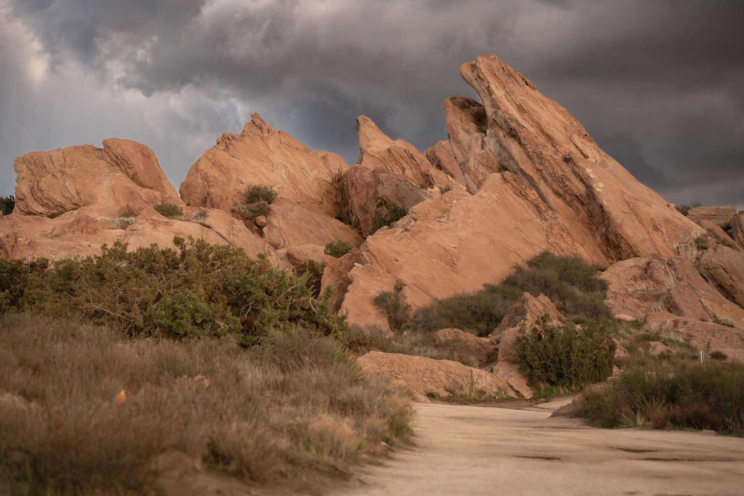 Desert landscape featuring dramatic red rock formations against cloudy sky.