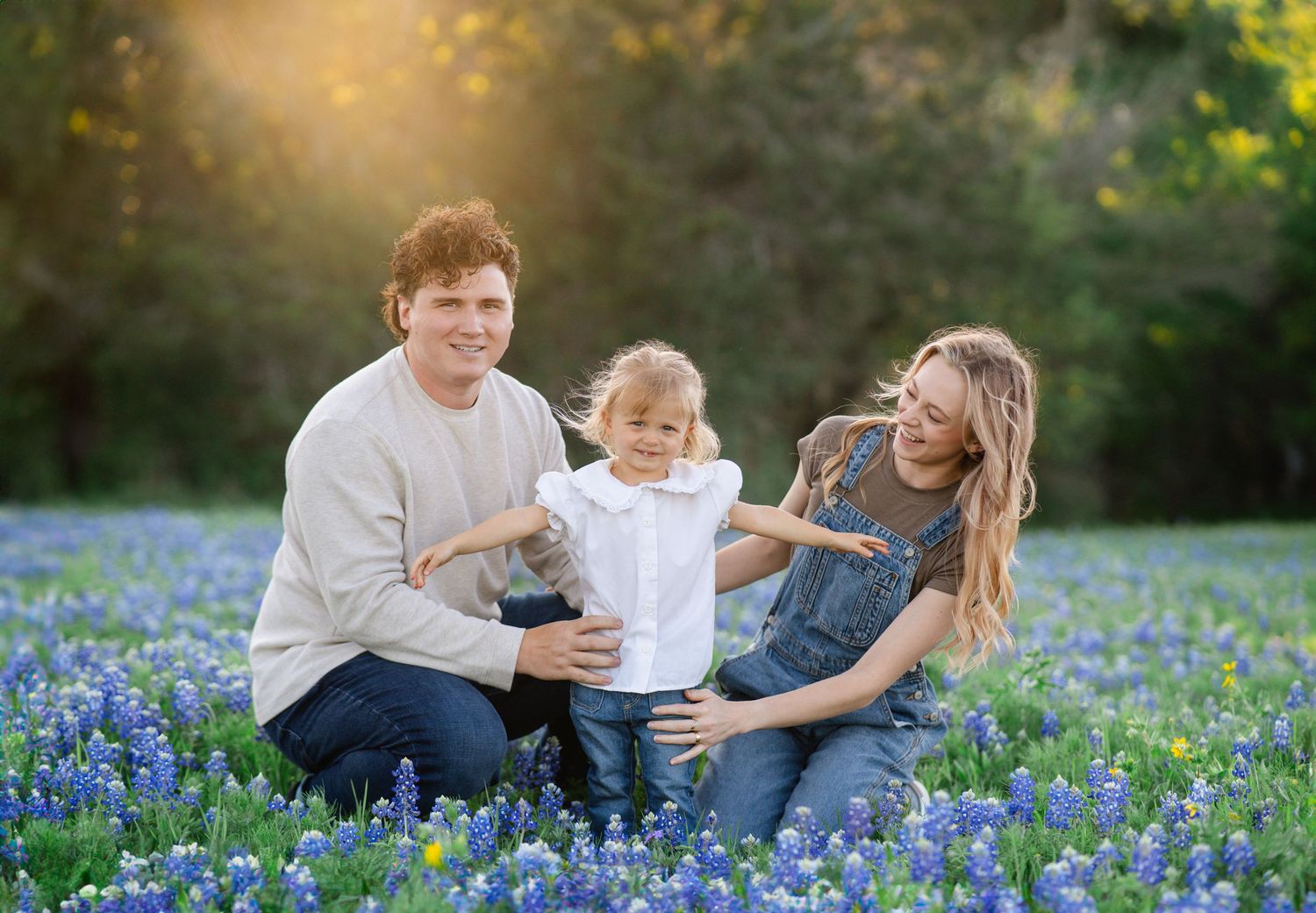 Family sitting together in a field of blooming bluebonnets during golden hour sunset.
