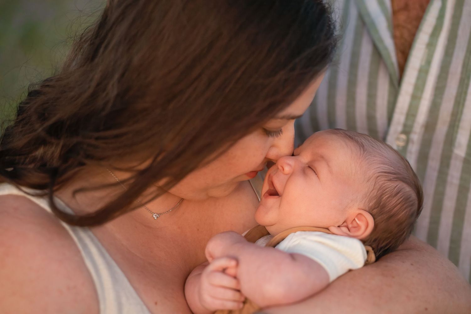 Parent tenderly kisses sleeping newborn baby while resting together on white bedding.