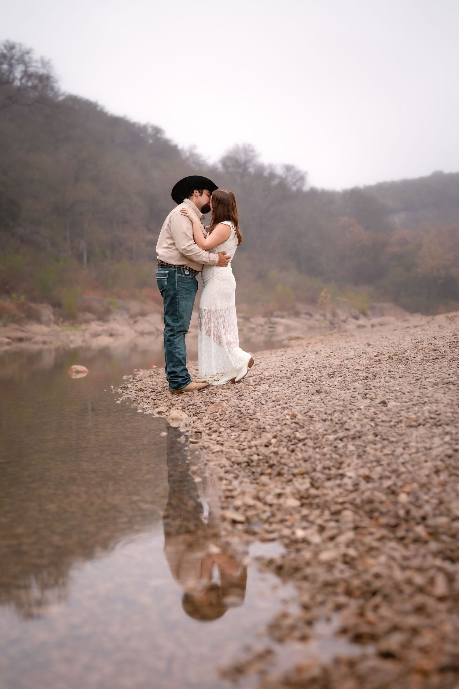A romantic couple shares a tender kiss by a rocky riverbank on a misty autumn day.