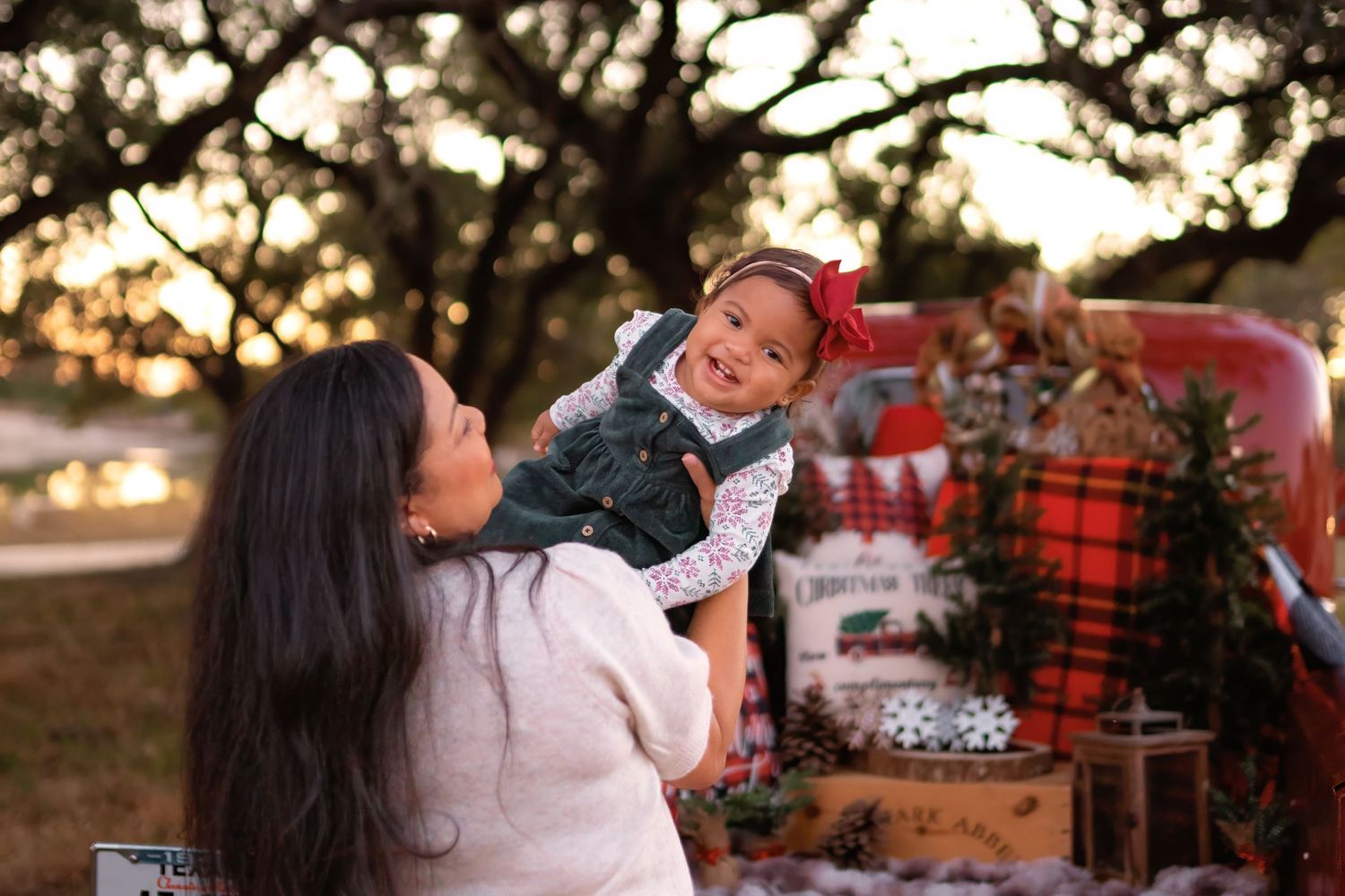 A mother lifts her smiling toddler in a festive Christmas outdoor photo session with a red truck backdrop.