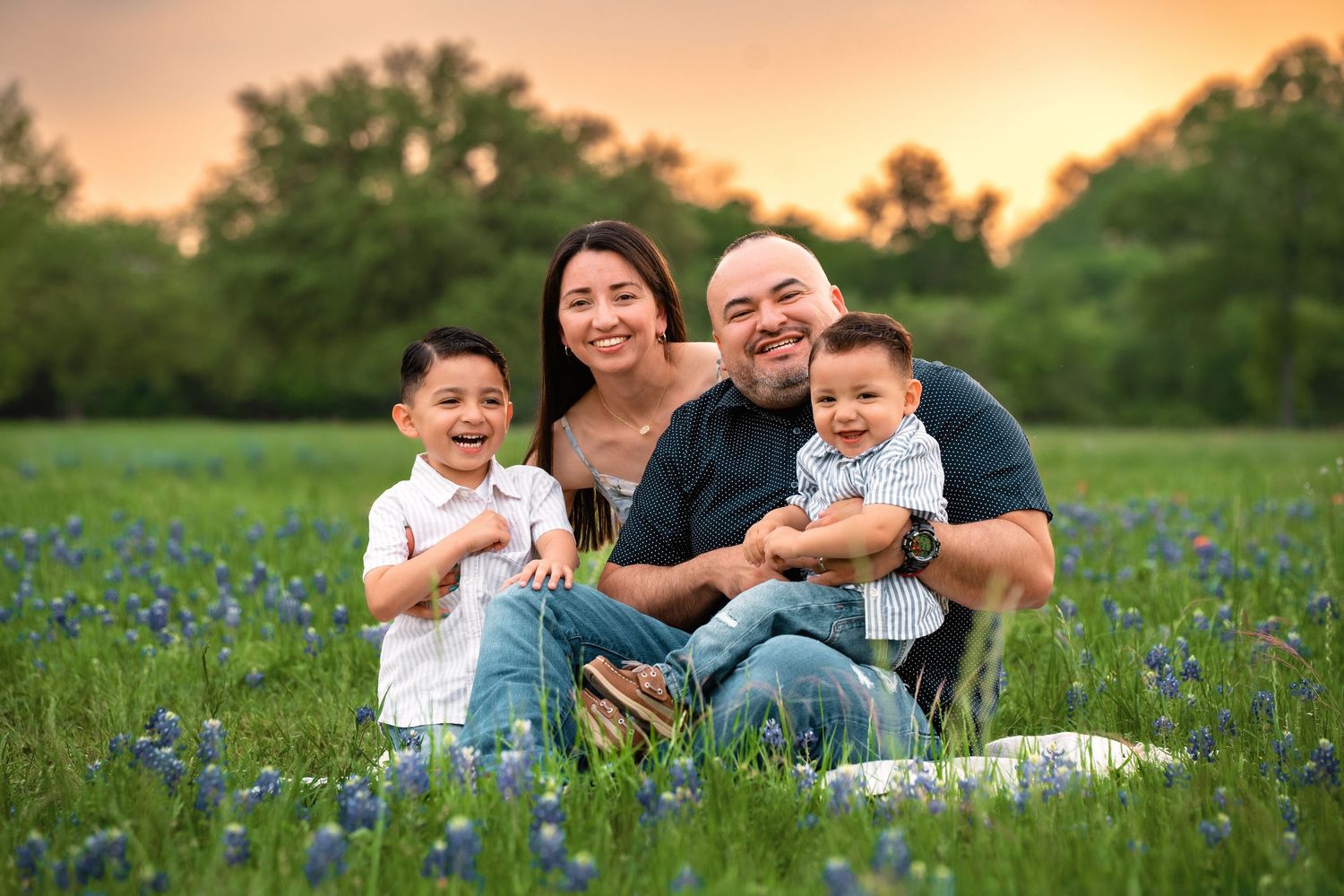 Family sits together in a field of Texas bluebonnets during sunset, capturing a warm family moment outdoors.