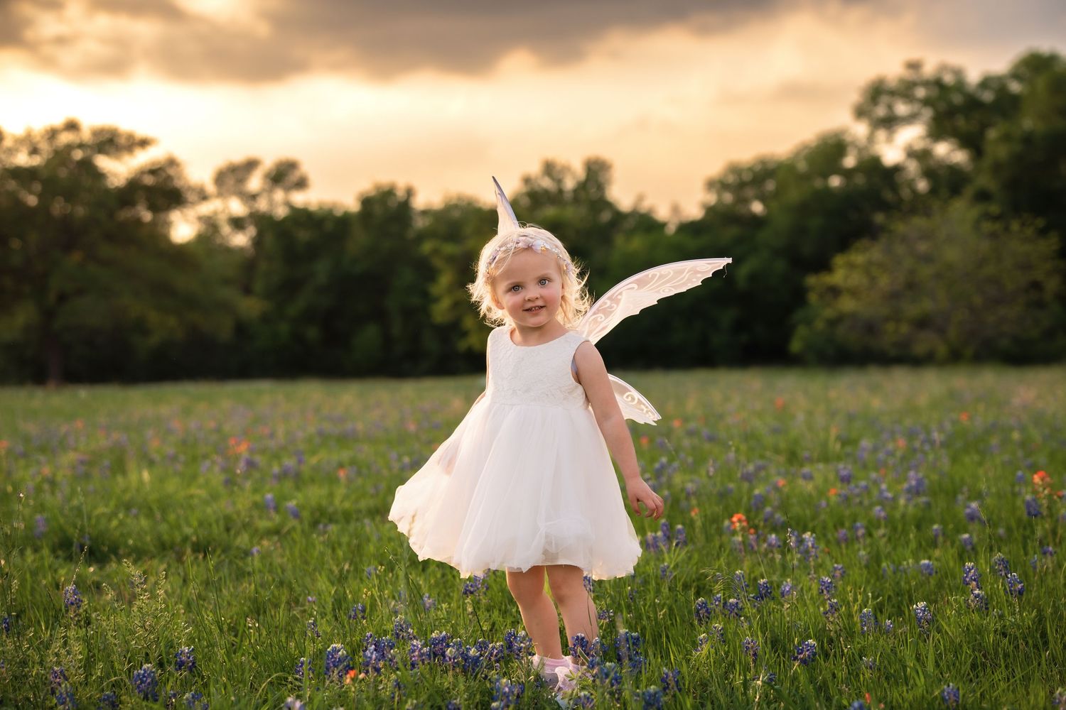 A child in a white dress twirls joyfully in a field of bluebonnets during golden hour.