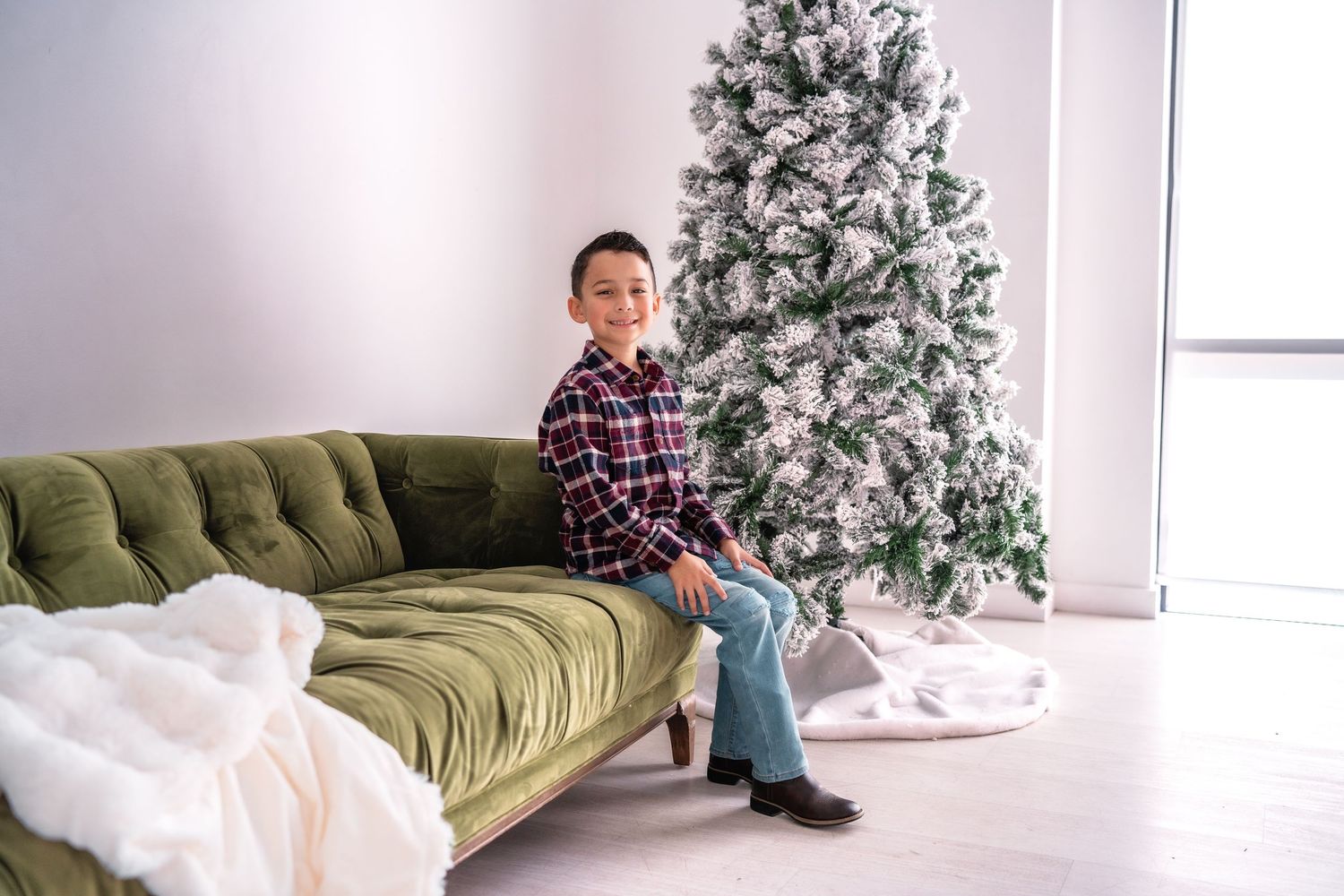 A minimalist holiday scene with decorative Christmas trees and a plush green velvet sofa against white walls.