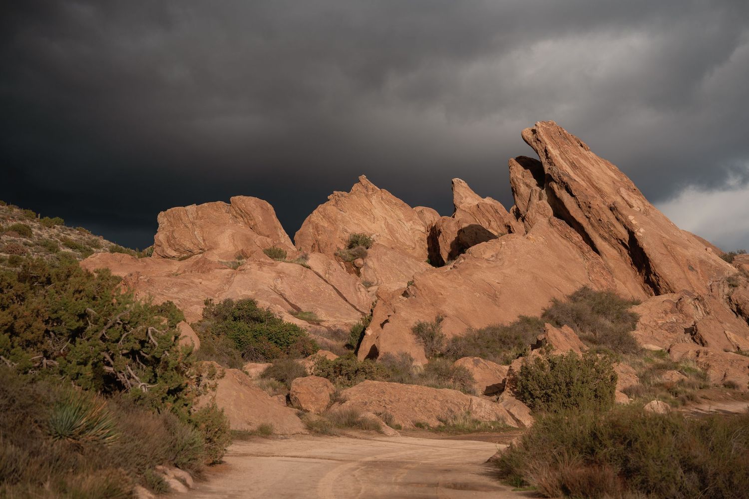 Dramatic red rock formations under stormy skies in desert landscape.