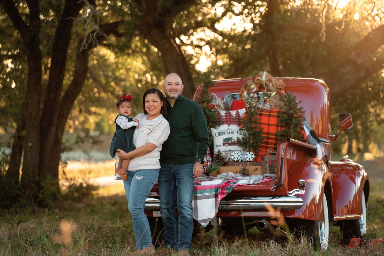 Vintage red truck decorated for Christmas with plaid blankets and silver ornaments in a sunlit forest setting.