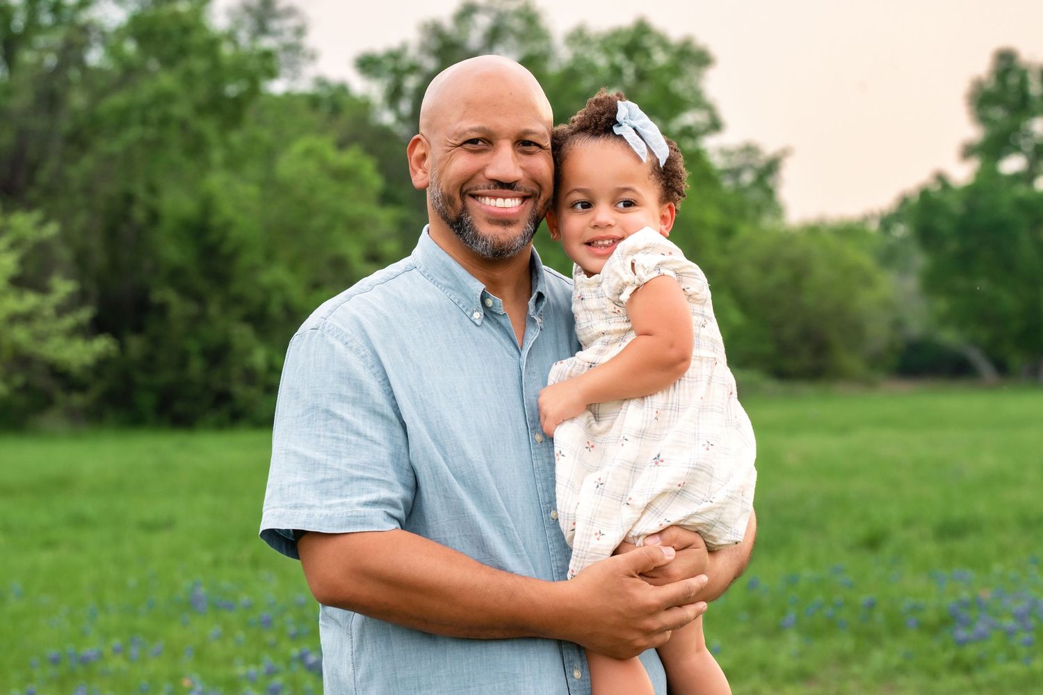 A parent and child share a joyful moment together while standing in a lush green field on a sunny day.