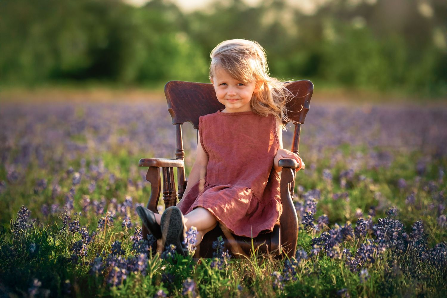A child sits in a vintage wooden chair amidst a beautiful field of blooming purple lavender flowers at sunset.