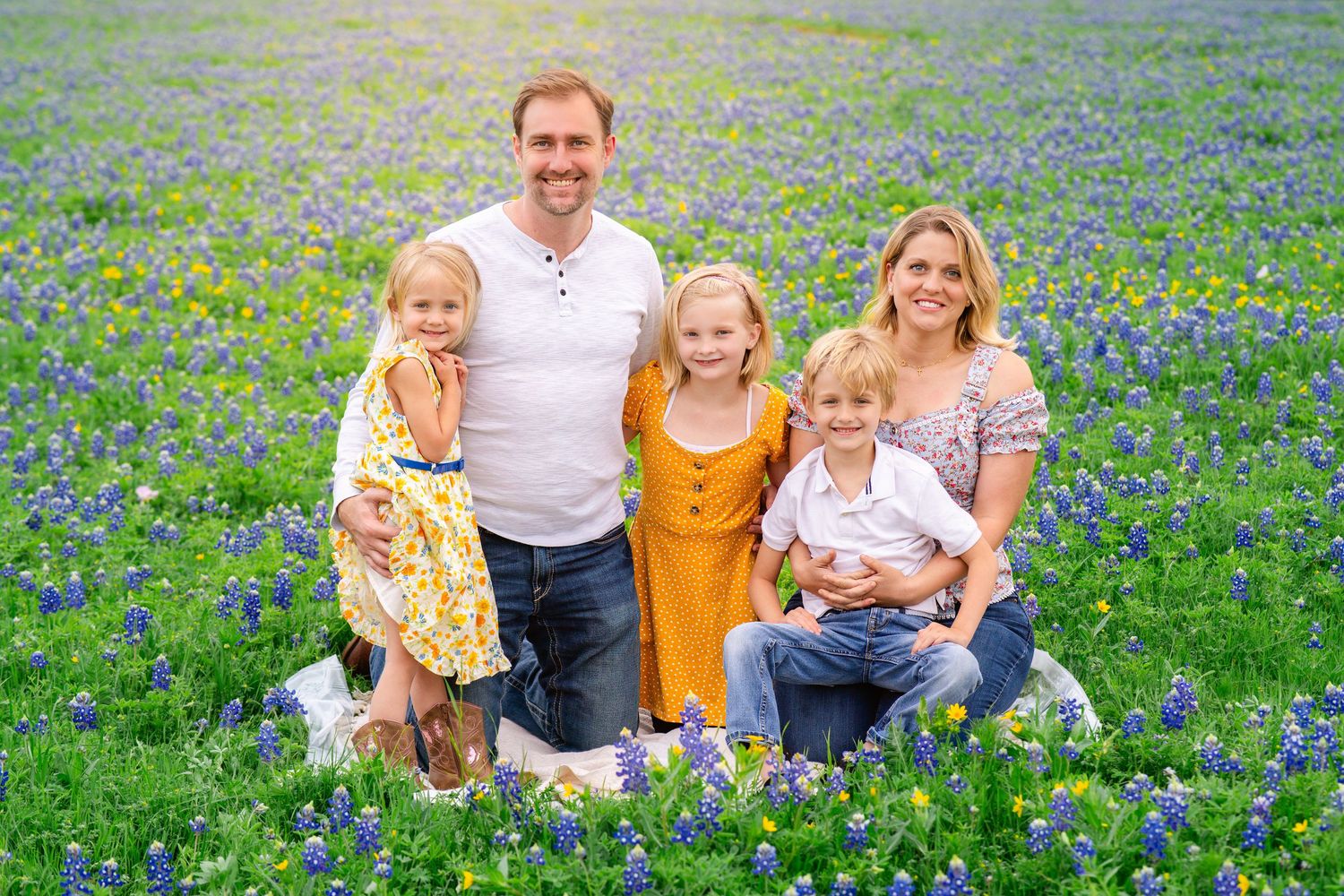 Family sits together in a blooming field of bluebonnets in Austin, TX while wearing casual clothing during a spring day.
