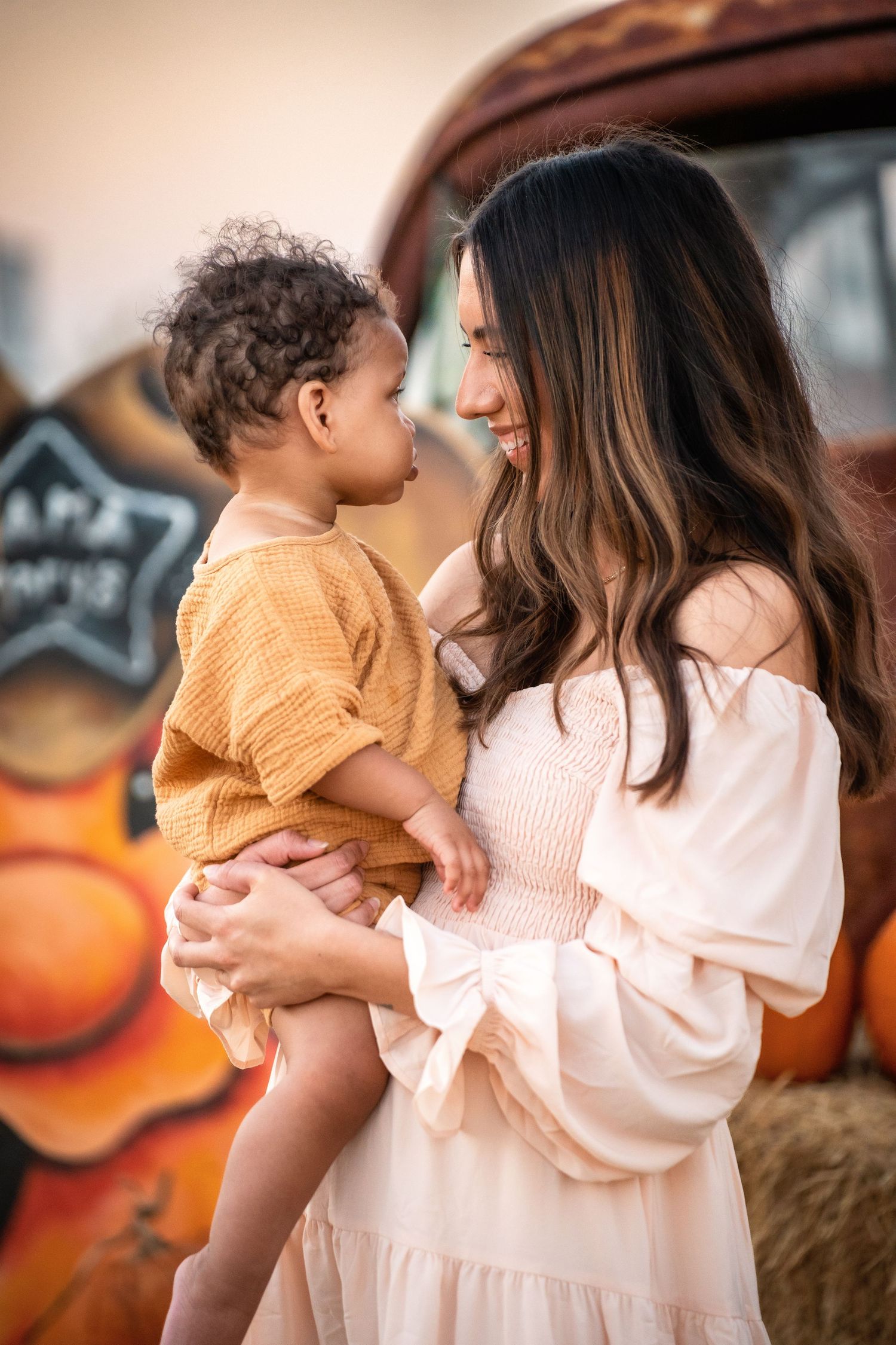 A mom in a white dress holds her baby in a series of sweet outdoor autumn scenes at Mama Mary's Pumpkin Patch in Creedmoor, TX