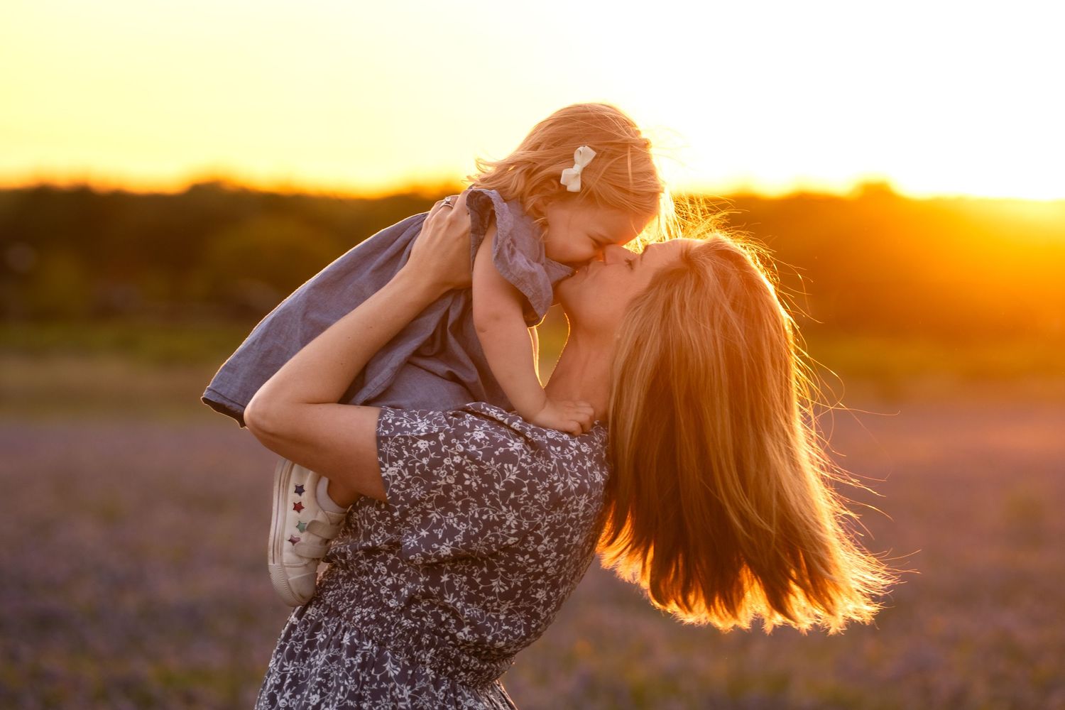 Woman in floral dress twirls her daughter gracefully in a golden bluebonnet field in Kyle, TX.