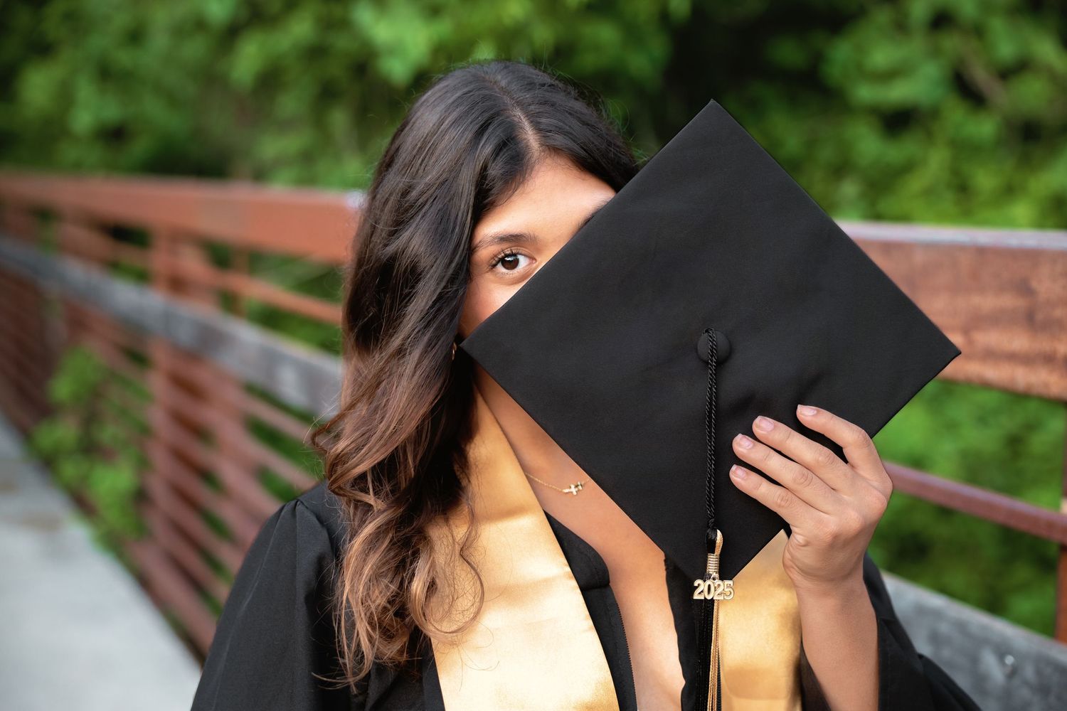 Someone laughs while hiding their face behind an open black graduation cap during an outdoor photoshoot.