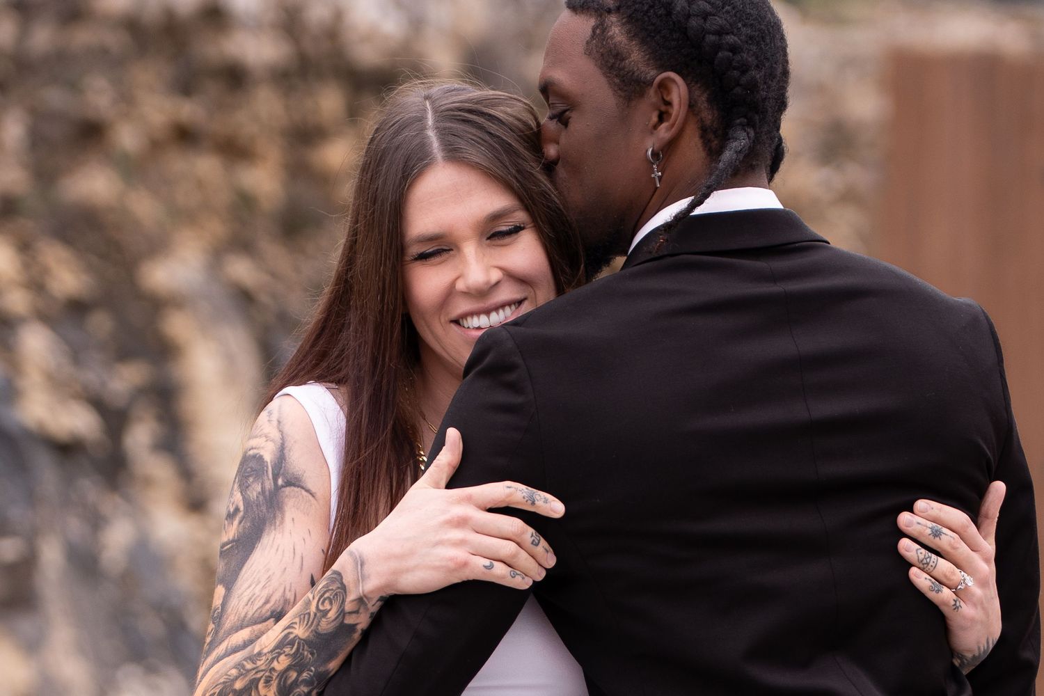 A couple shares a tender embrace during their wedding with the bride showing a sleeve tattoo.