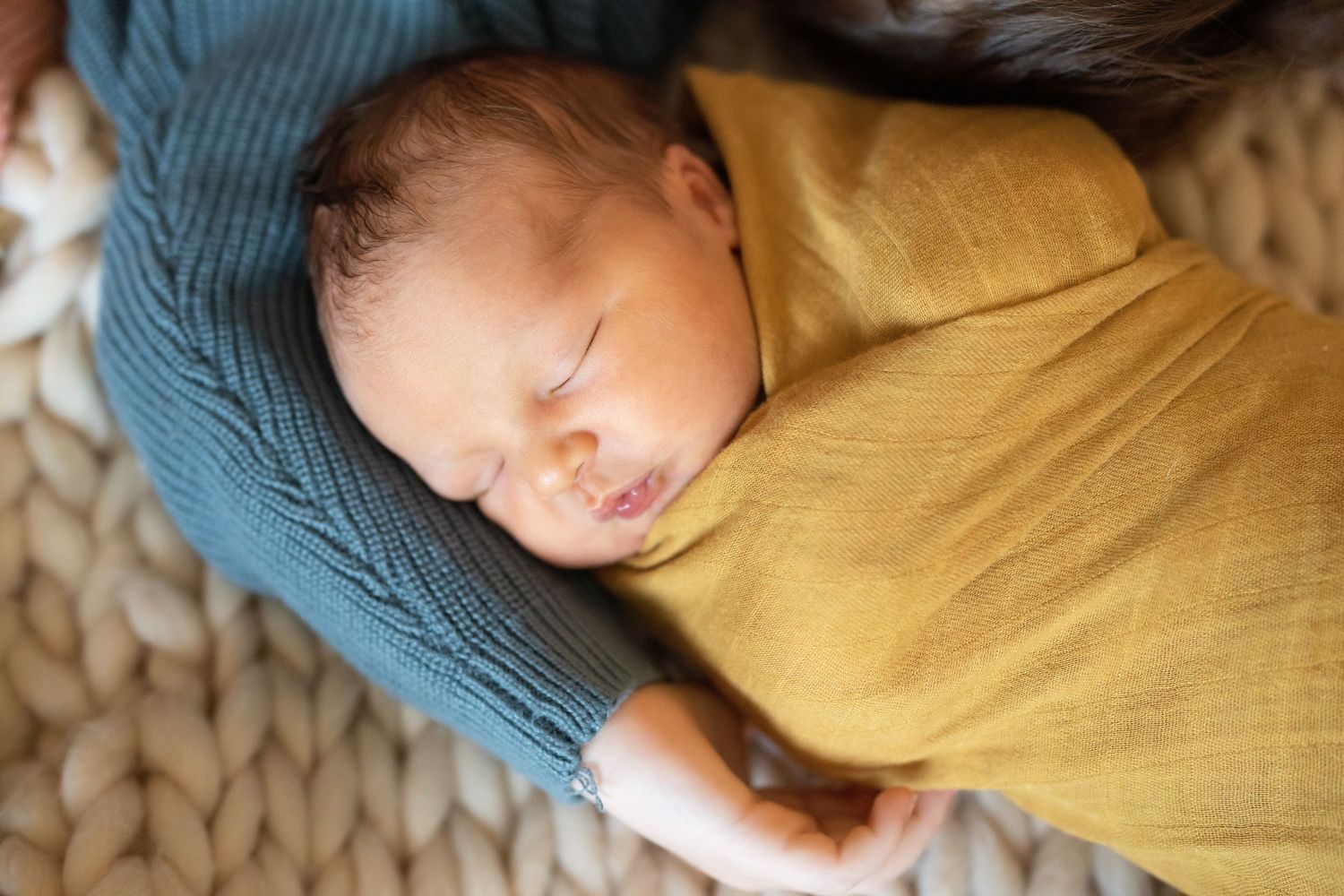 Newborn baby sleeping peacefully swaddled in a mustard yellow wrap, resting in a cozy basket.