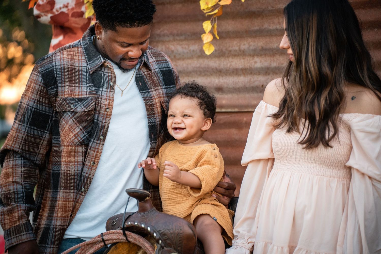 A family enjoying an autumn photoshoot outdoors with falling golden leaves.