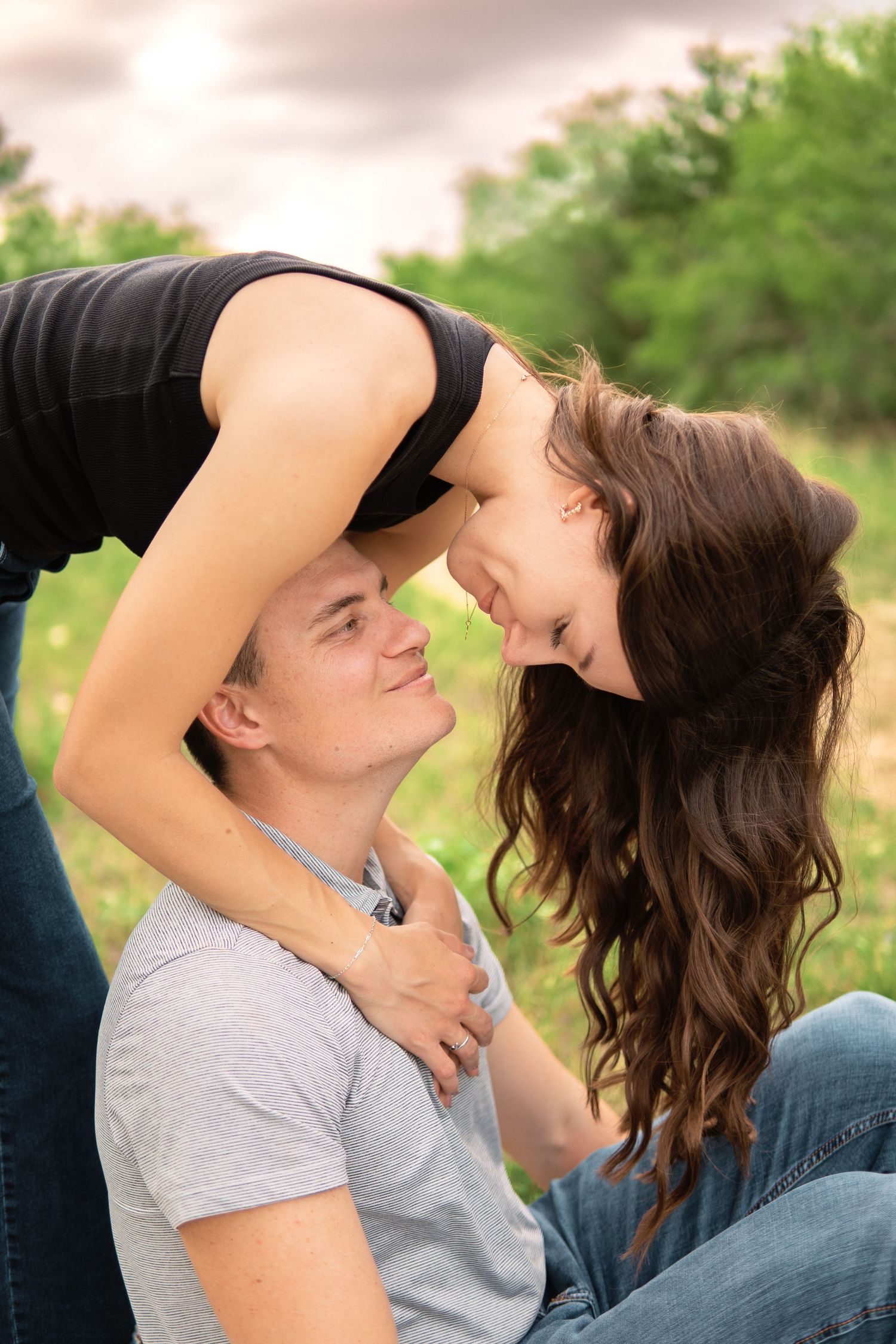 Young couple sharing a romantic moment outdoors, woman leaning over man in a green field.