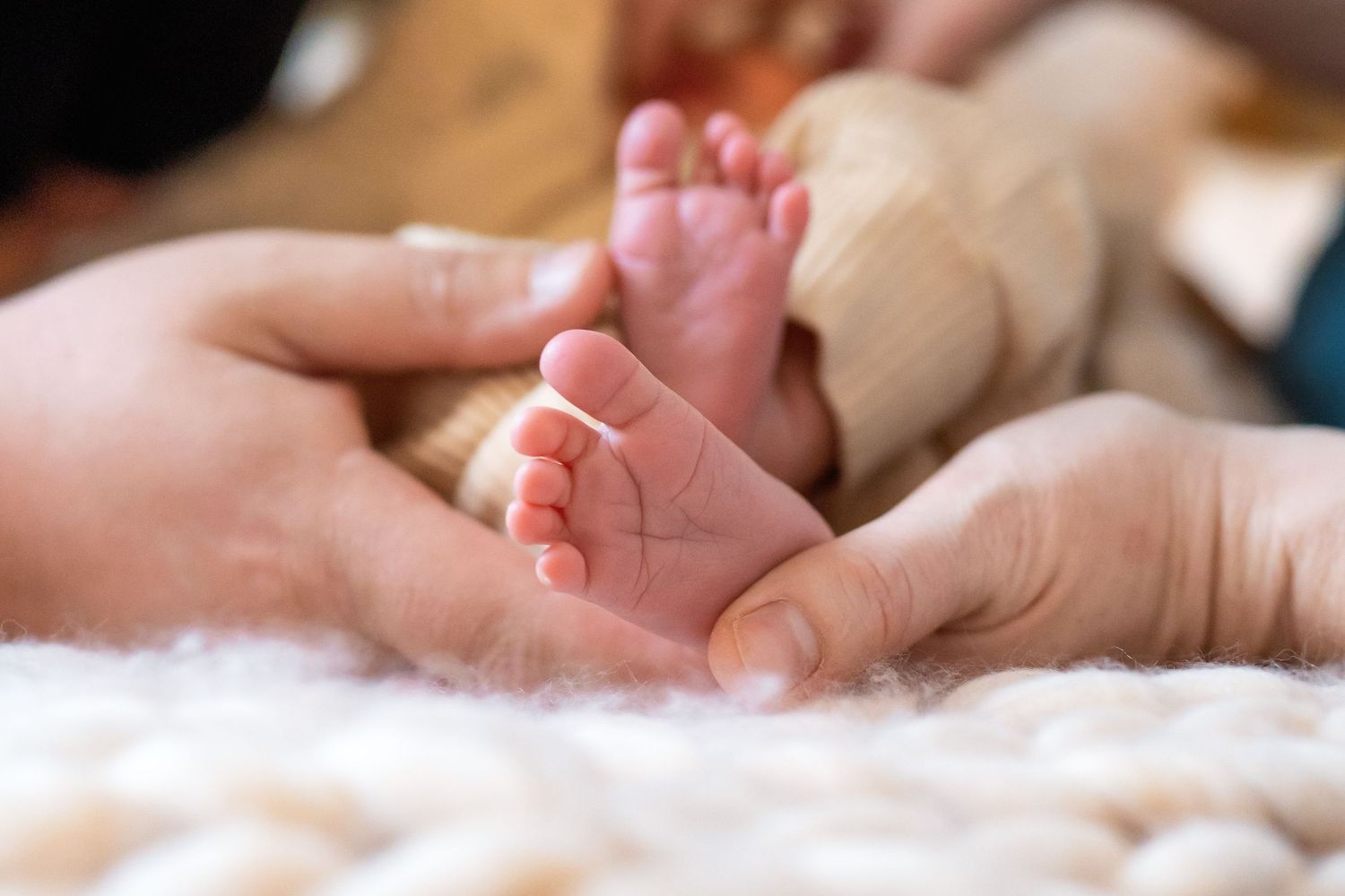 Close up of gentle newborn baby hands on soft white blanket.