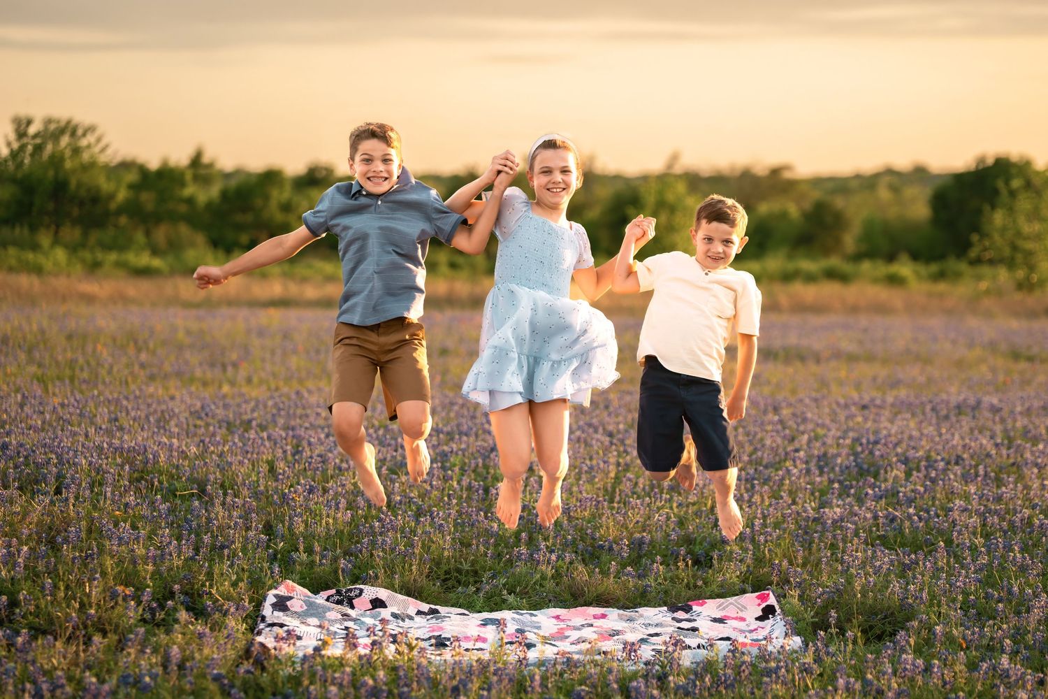 Children playing and jumping on a picnic blanket in a beautiful purple wildflower field at sunset.