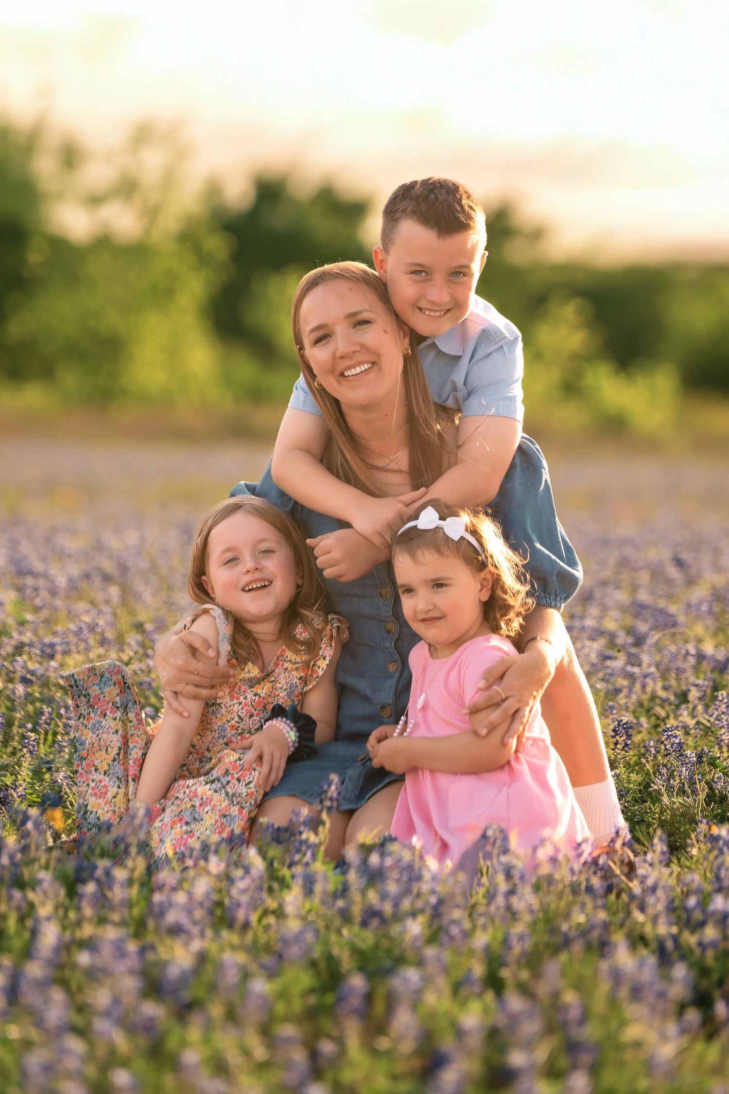 A happy family sits together in a blooming purple wildflower field during golden hour sunset.