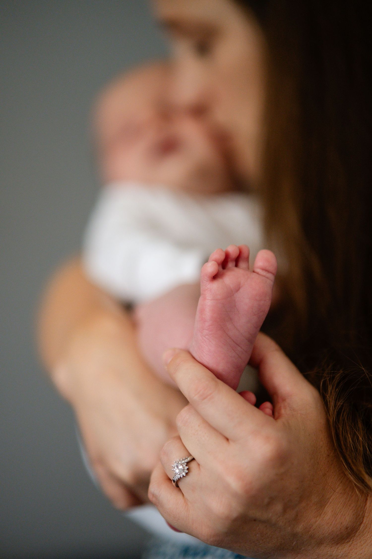 Close-up of a mother holding her newborn baby's tiny feet, wearing a diamond engagement ring.
