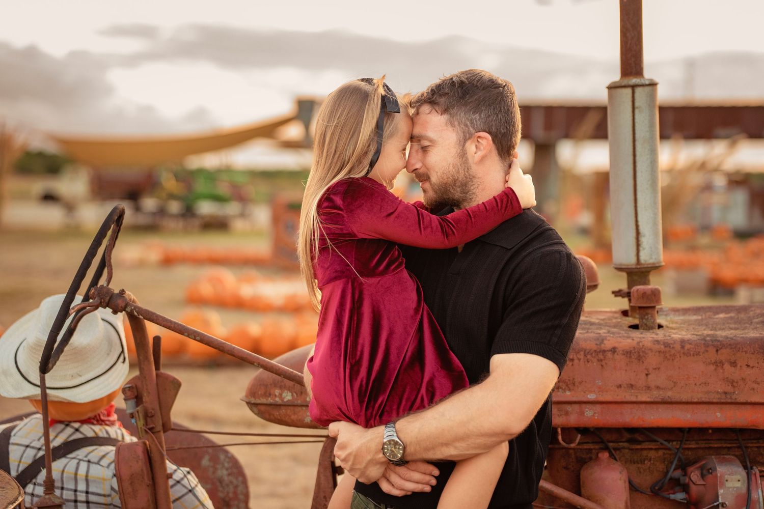 Couple sharing a romantic moment near a vintage tractor at a pumpkin patch during golden hour.