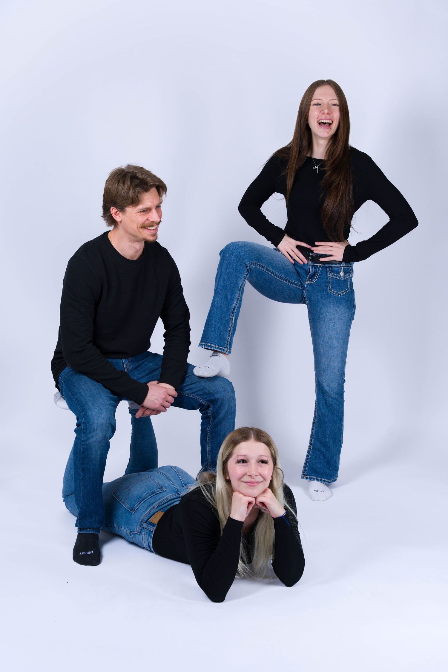 Two people in black tops and blue jeans pose playfully against a white backdrop in a photo series.