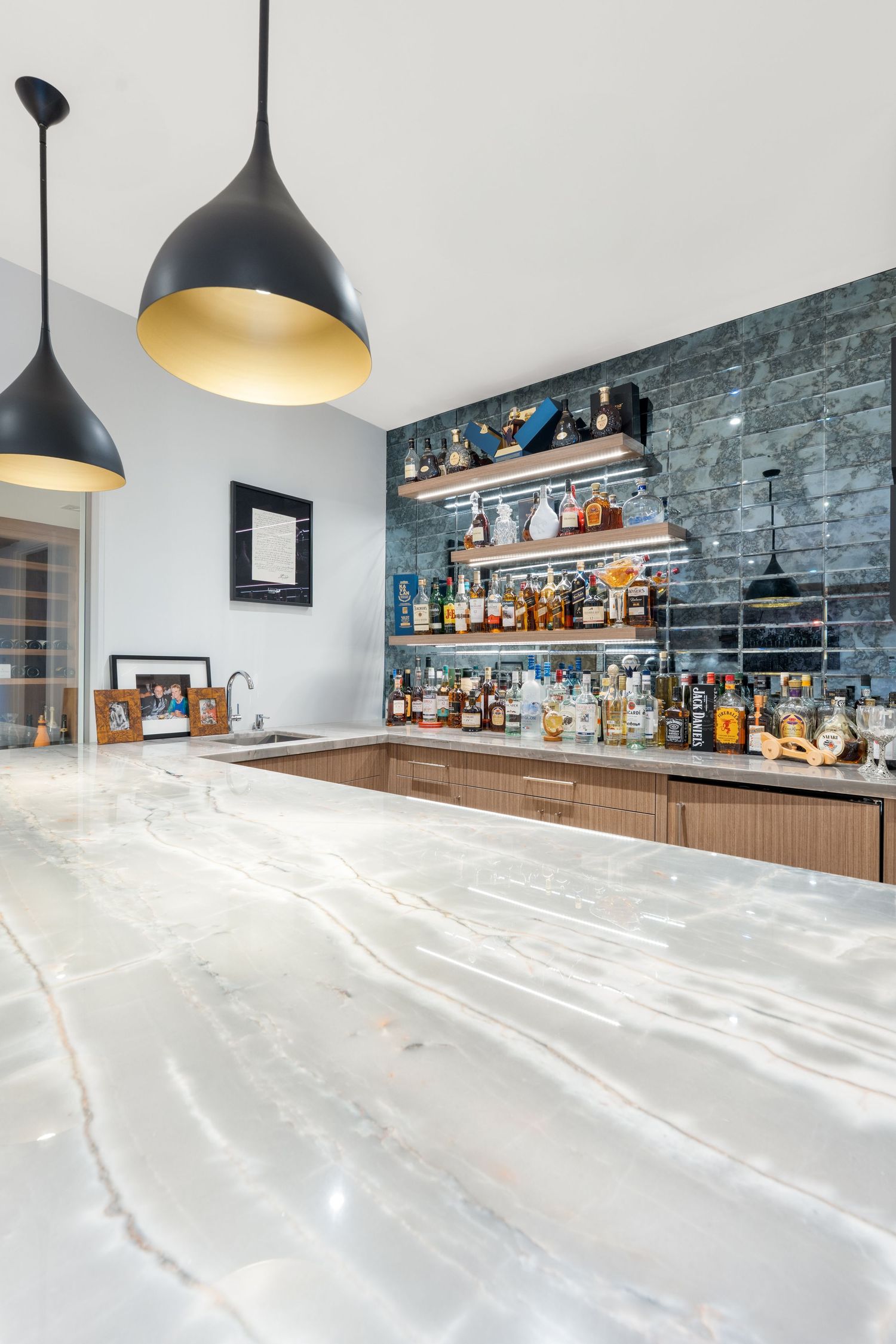 Contemporary bar area featuring sleek marble countertop and black pendant lights with bottle display.
