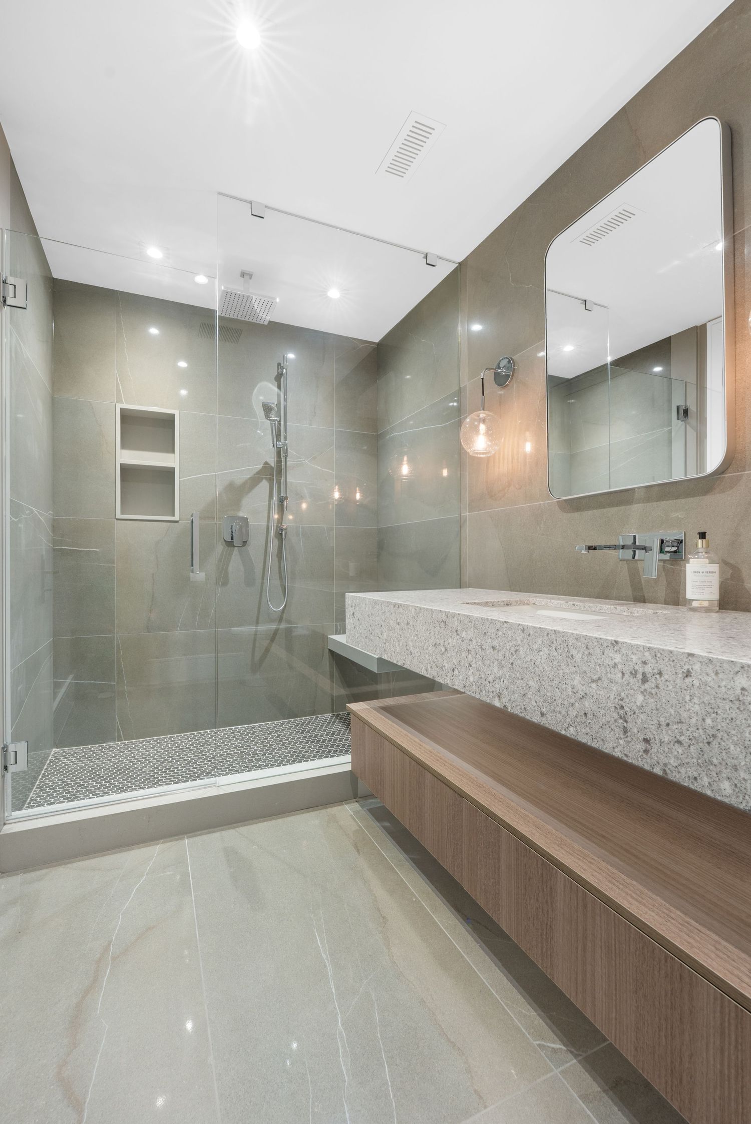 Modern bathroom featuring sleek grey tiles, wooden vanity, and glass shower enclosure with contemporary fixtures.