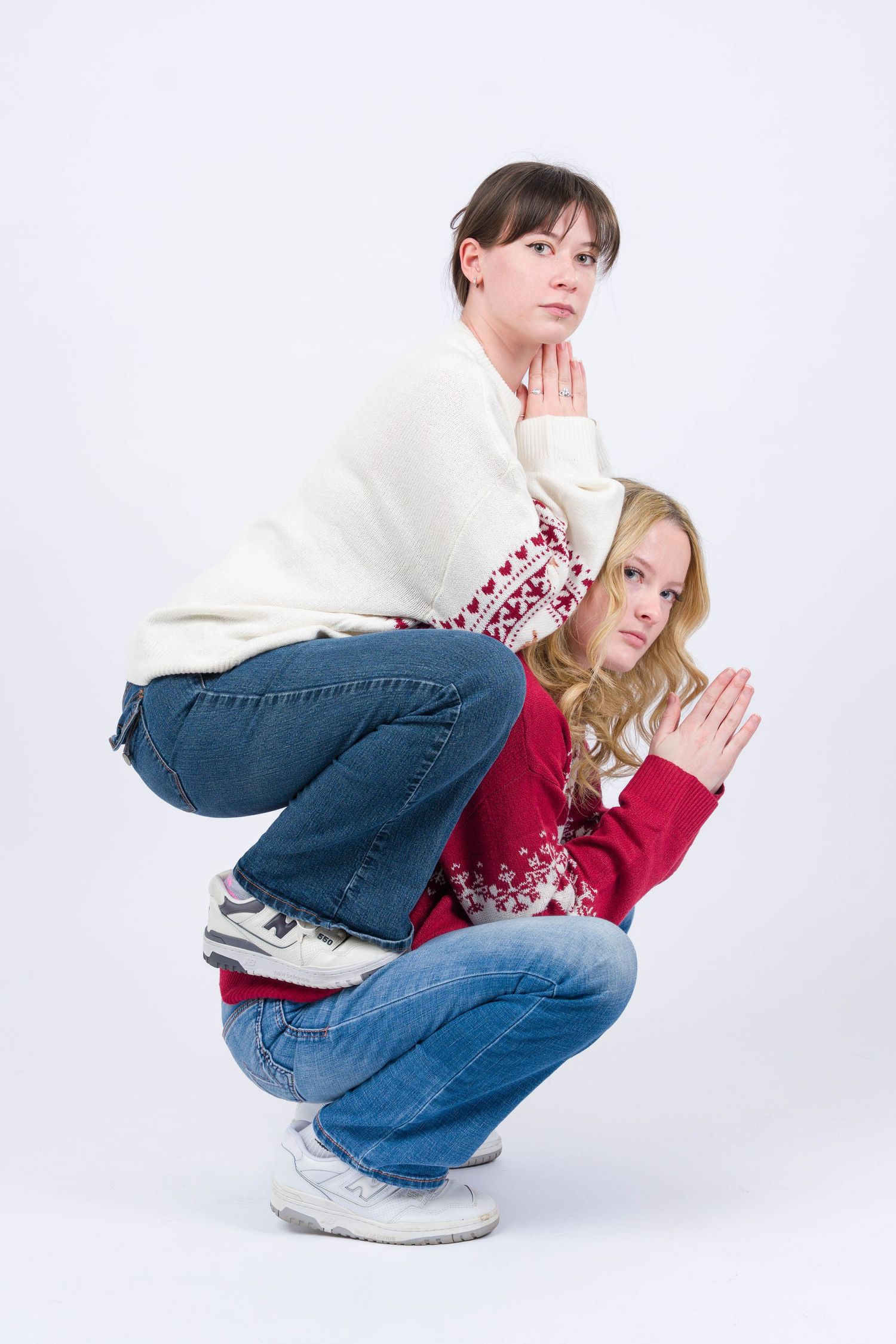 Two people in casual winter wear crouching back to back against white background wearing jeans and sweaters.