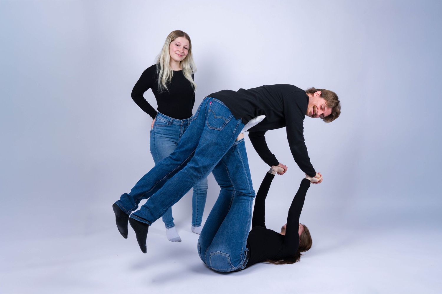 Two people in matching denim jeans strike playful poses against a light gray studio backdrop.