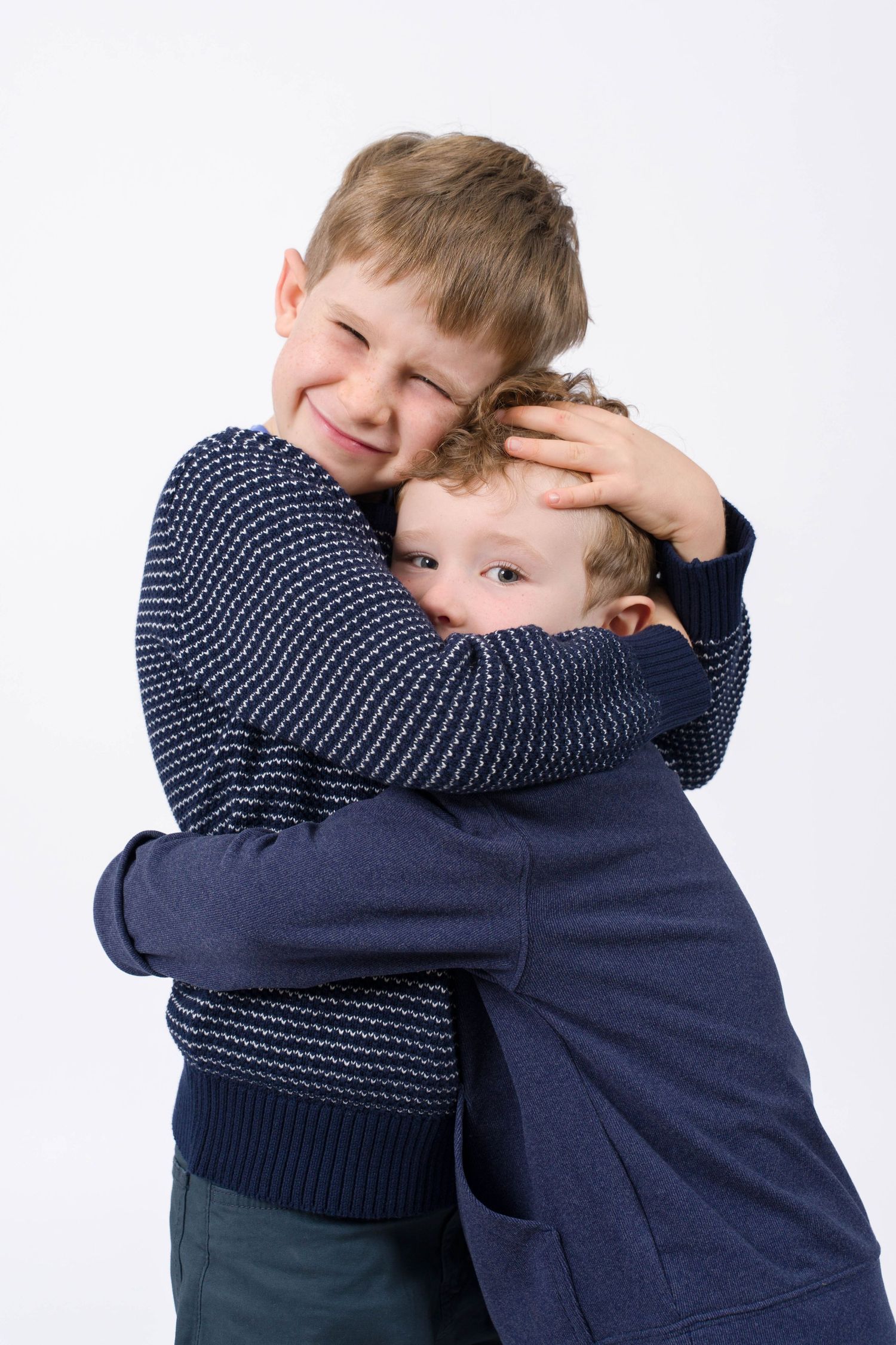 Three candid photos showing two young children in navy blue sweaters sharing warm embraces against a white background.