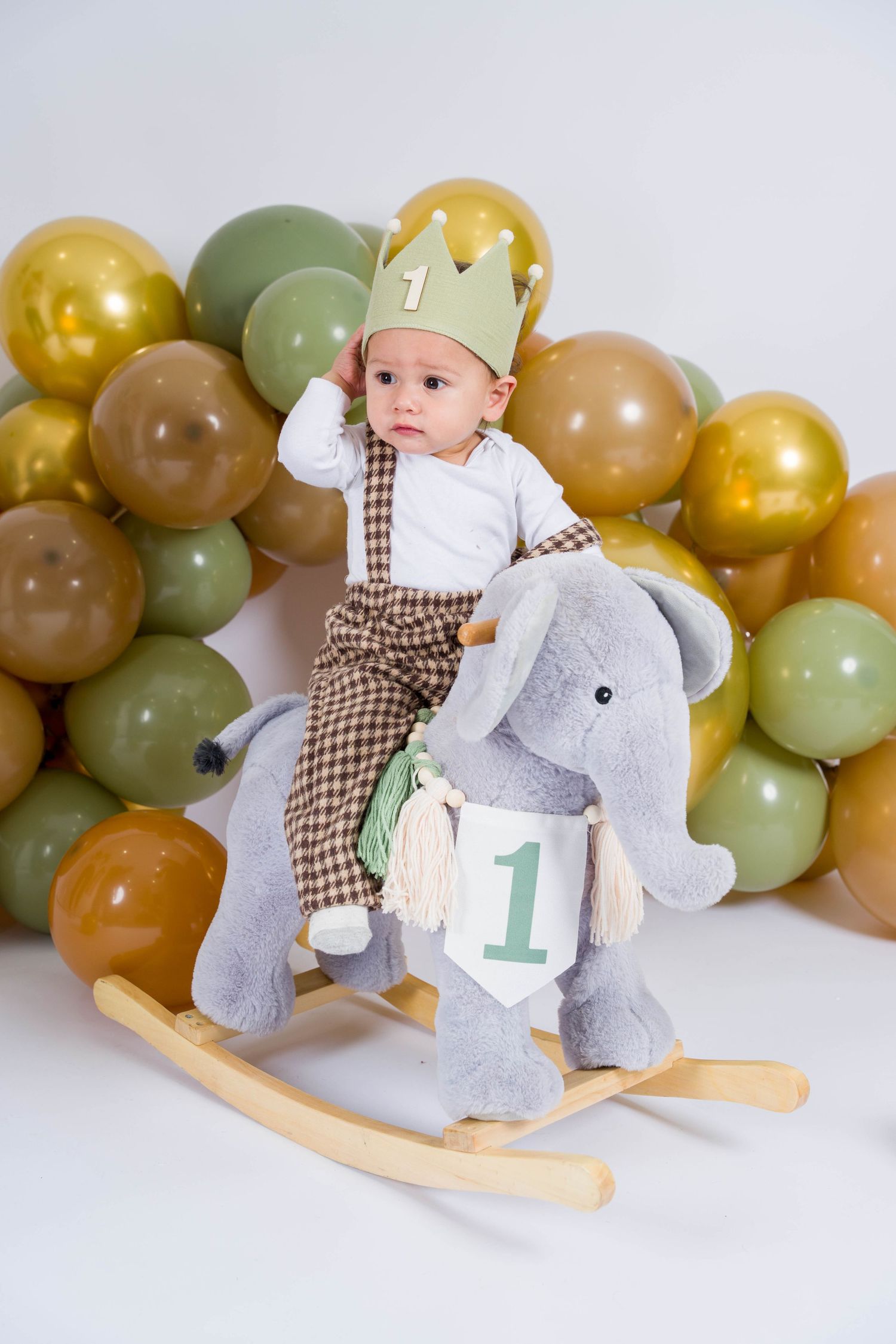 Wooden rocking horse decorated with balloons in muted earth tones creates a charming first birthday photo setting.