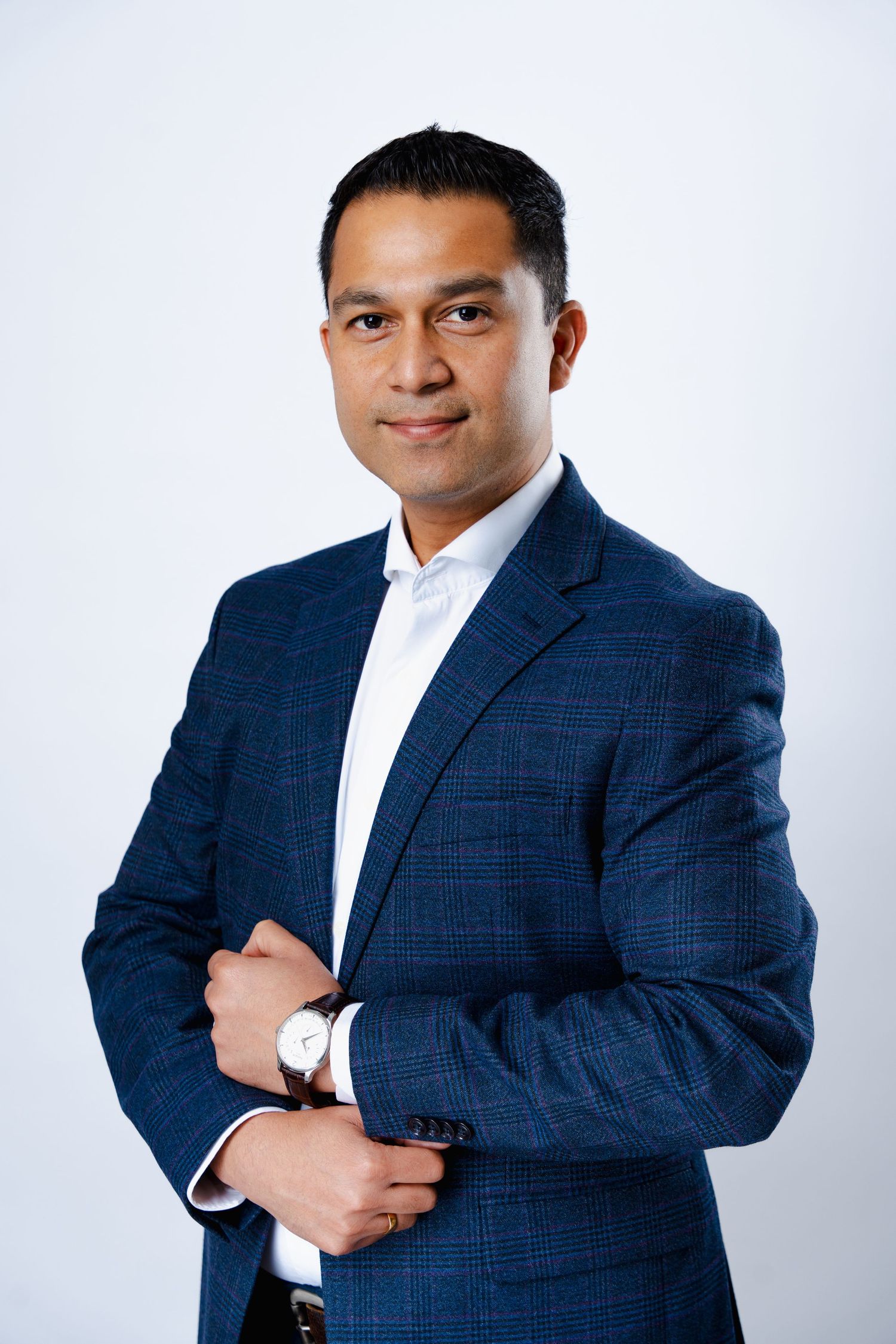 Professional portrait of a person in a navy blue checkered suit and white shirt posing against a light background.