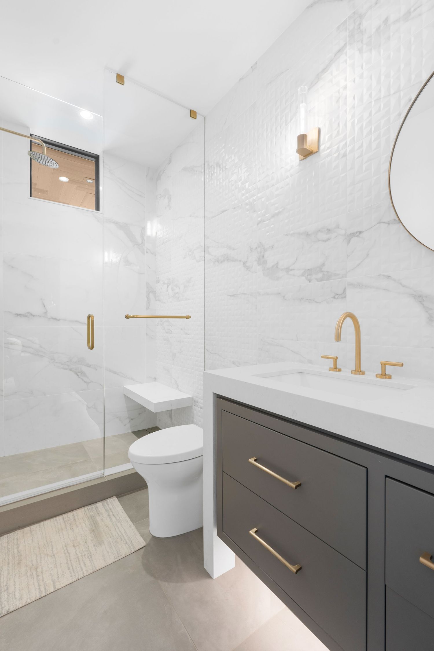 Modern bathroom interior with white marble walls, dark vanity cabinet, and gold fixtures.