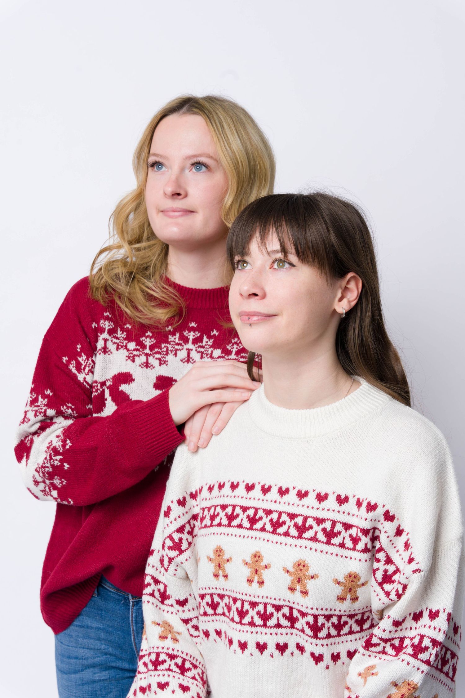 Two people wearing festive holiday sweaters with gingerbread and Nordic patterns pose together against a white background.