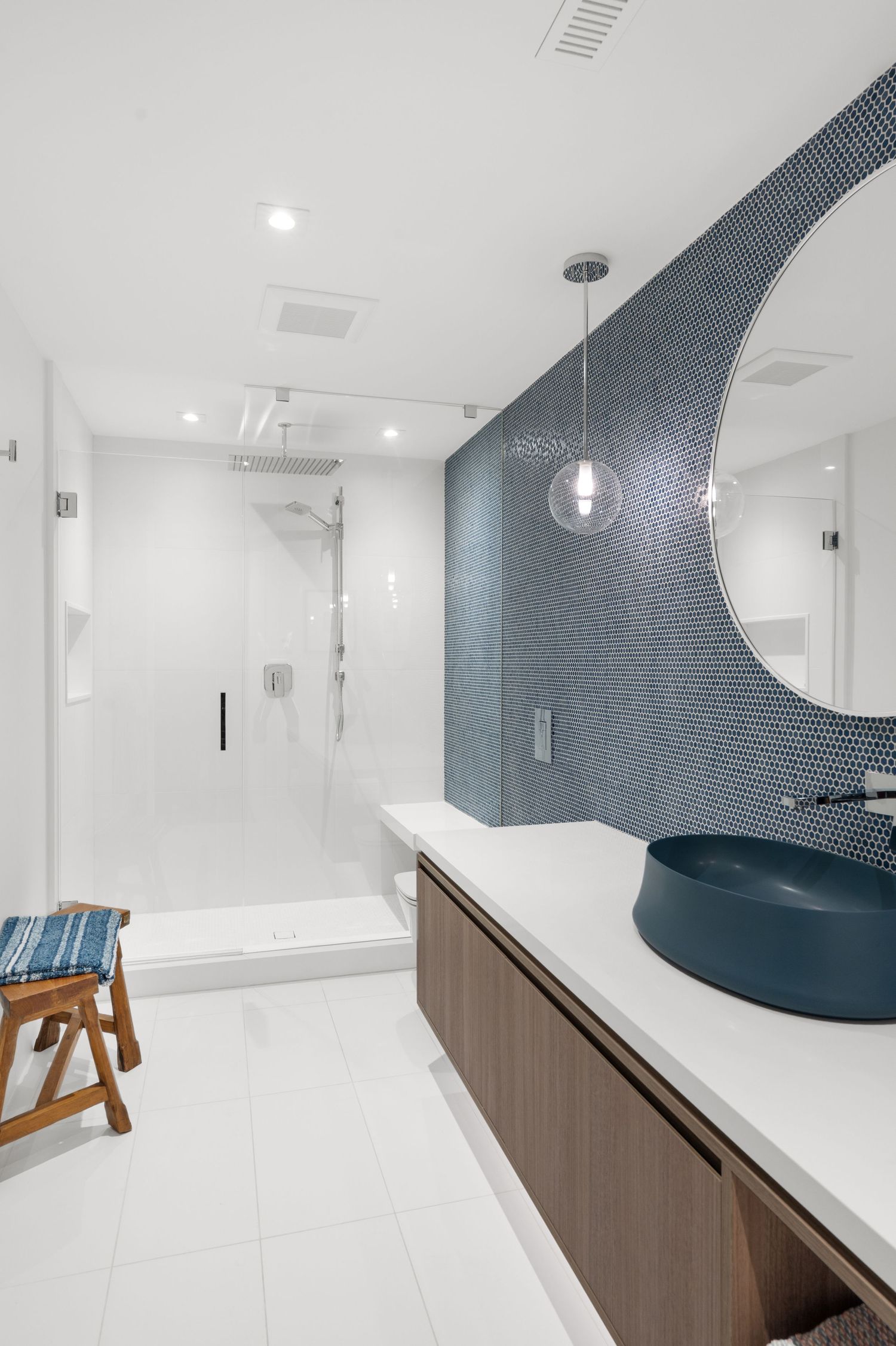 Modern bathroom with blue mosaic tile accent wall and wooden vanity in clean white design.