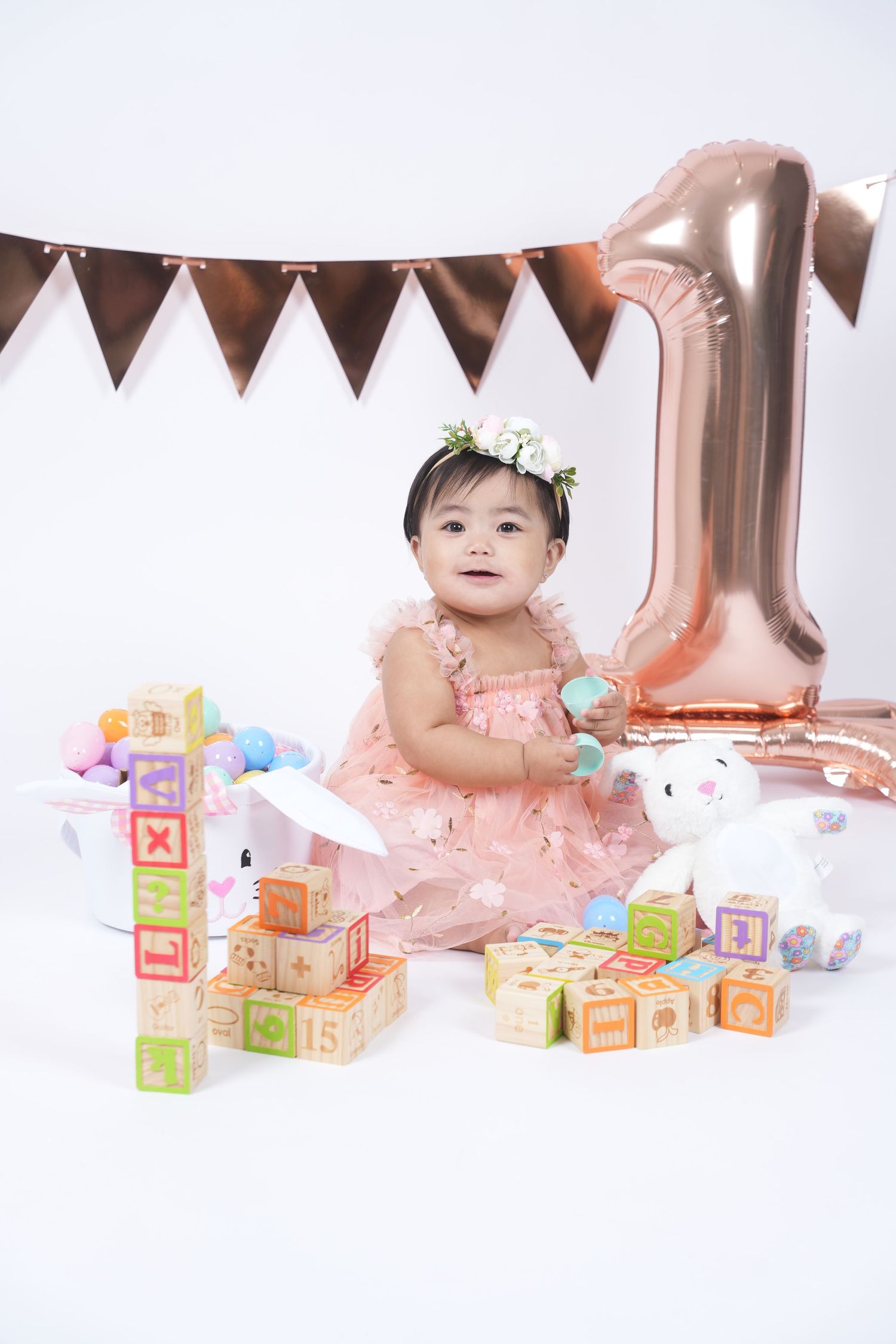 Baby sitting with colorful alphabet blocks and rose gold decorations for first birthday photo session.