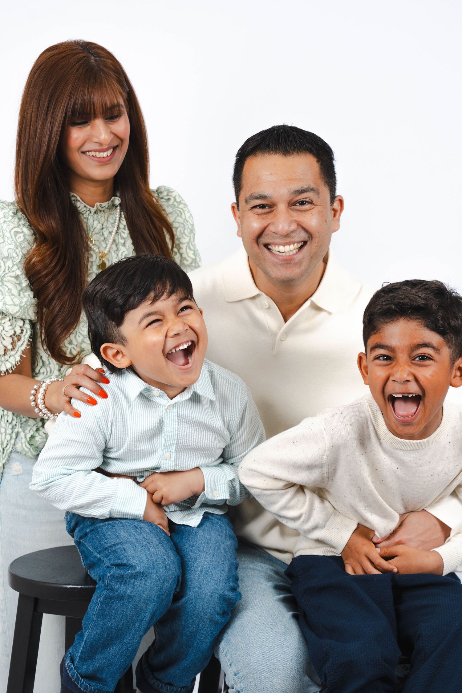 A happy family wearing white shirts and jeans laughs together while sitting and posing for a casual portrait.