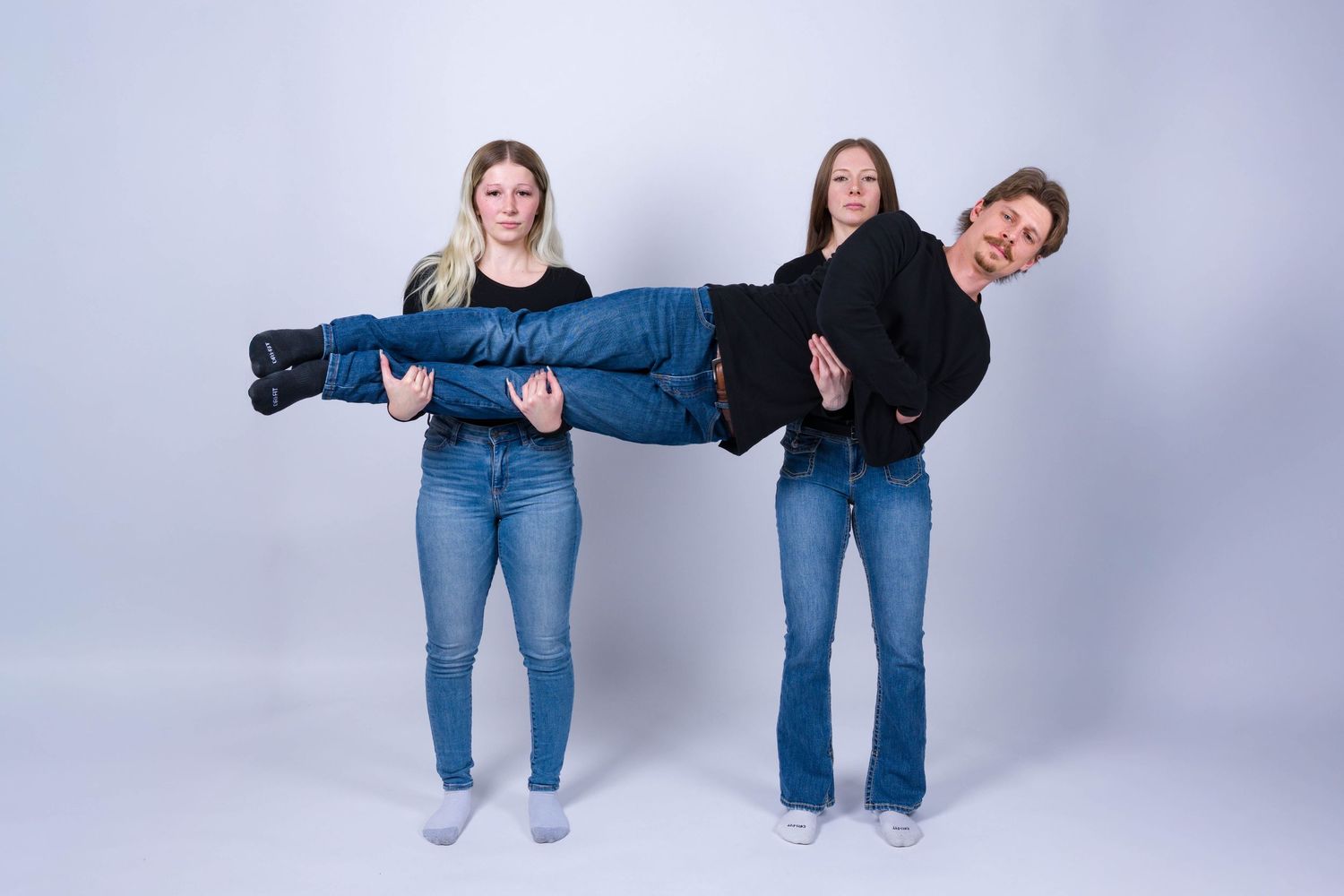 People in matching blue jeans perform playful poses against a light gray studio backdrop.