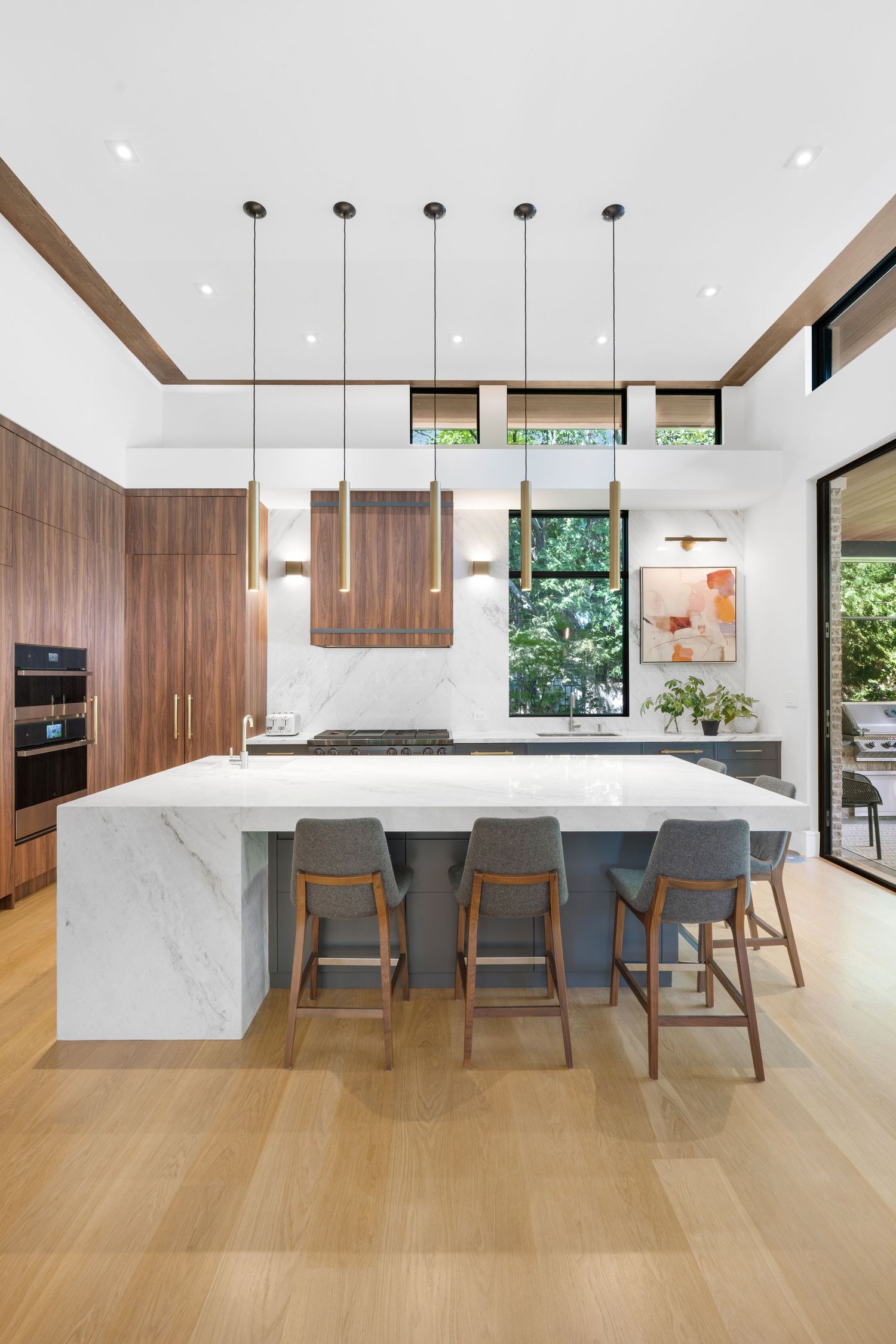 Contemporary open kitchen with marble island, walnut cabinetry, and pendant lighting over breakfast bar seating.