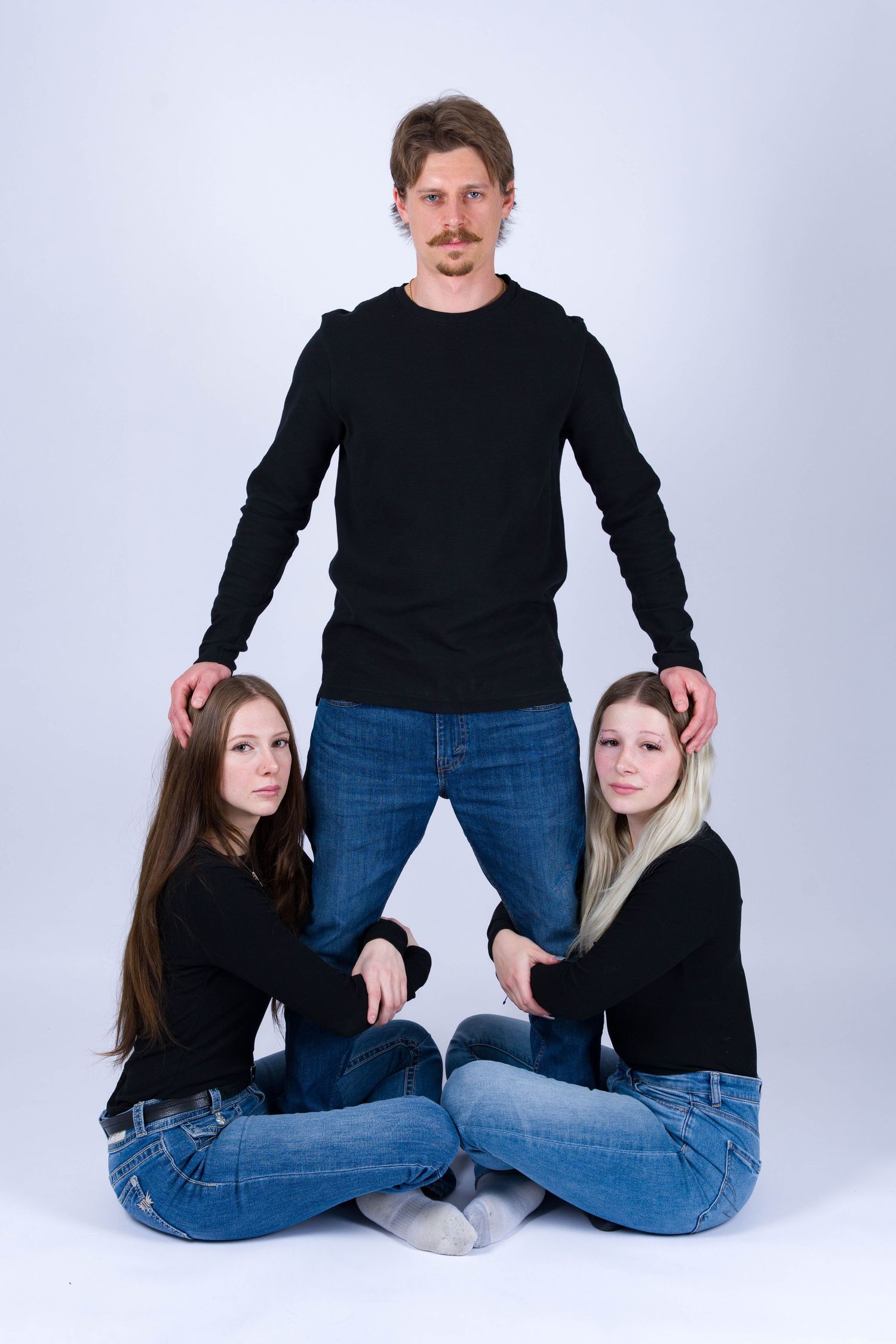 Three people in matching black tops and jeans pose together in a studio setting against a light backdrop.