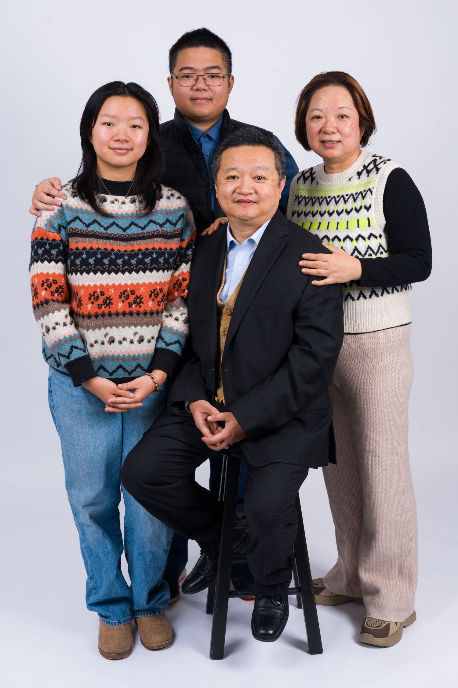 A group poses together wearing winter sweaters with fair isle patterns against a white studio background.
