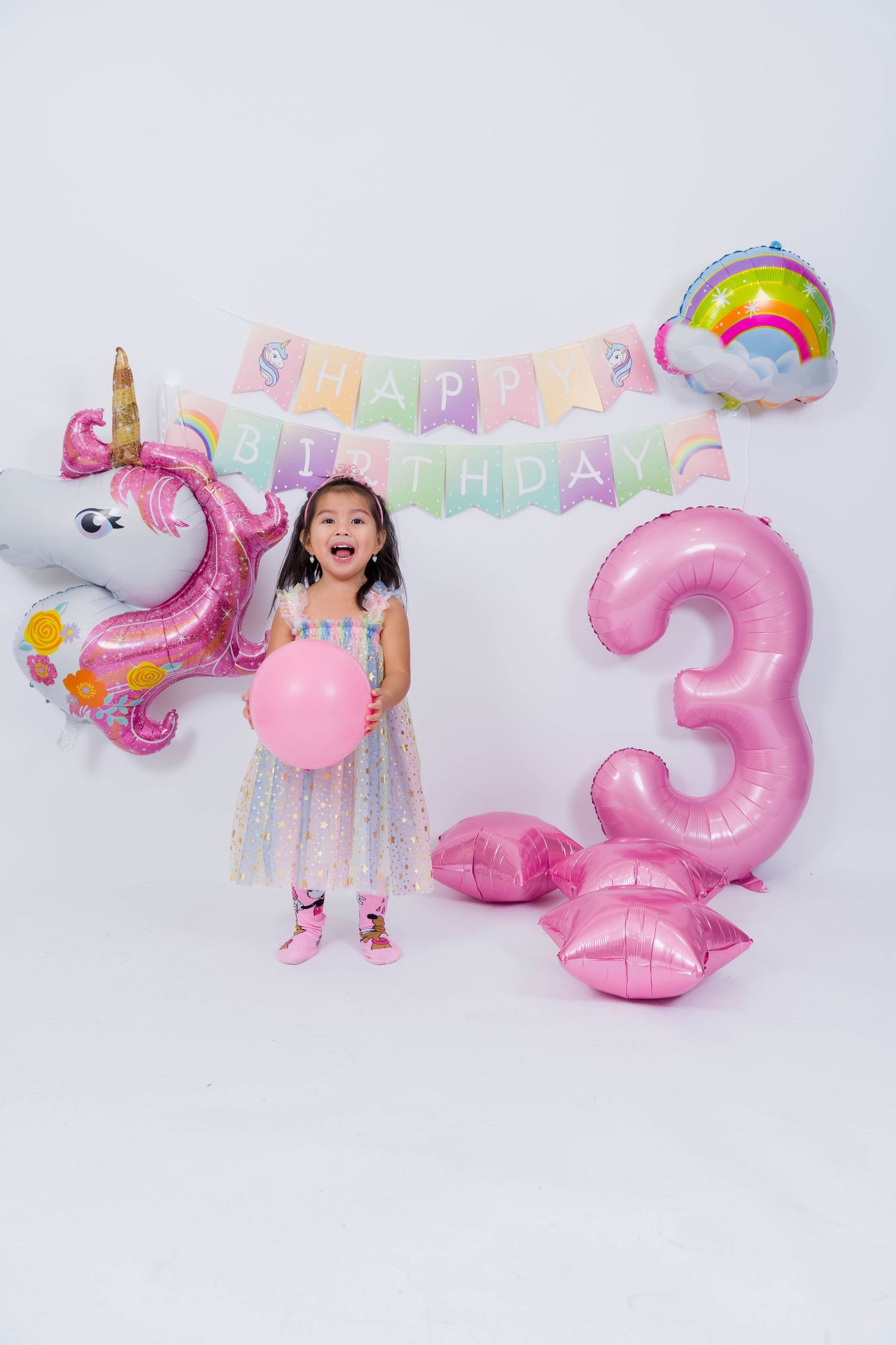 Collage of pink birthday party decorations including balloons, banners, and number three for a child's celebration.