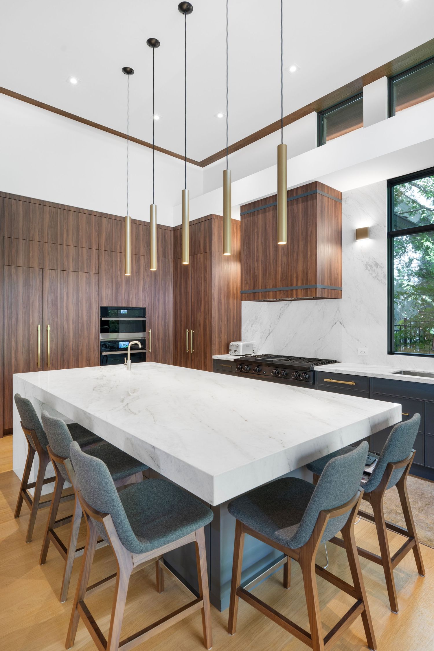 Elegant dining area with teal chairs, marble table, and modern pendant lights in an open-concept space.