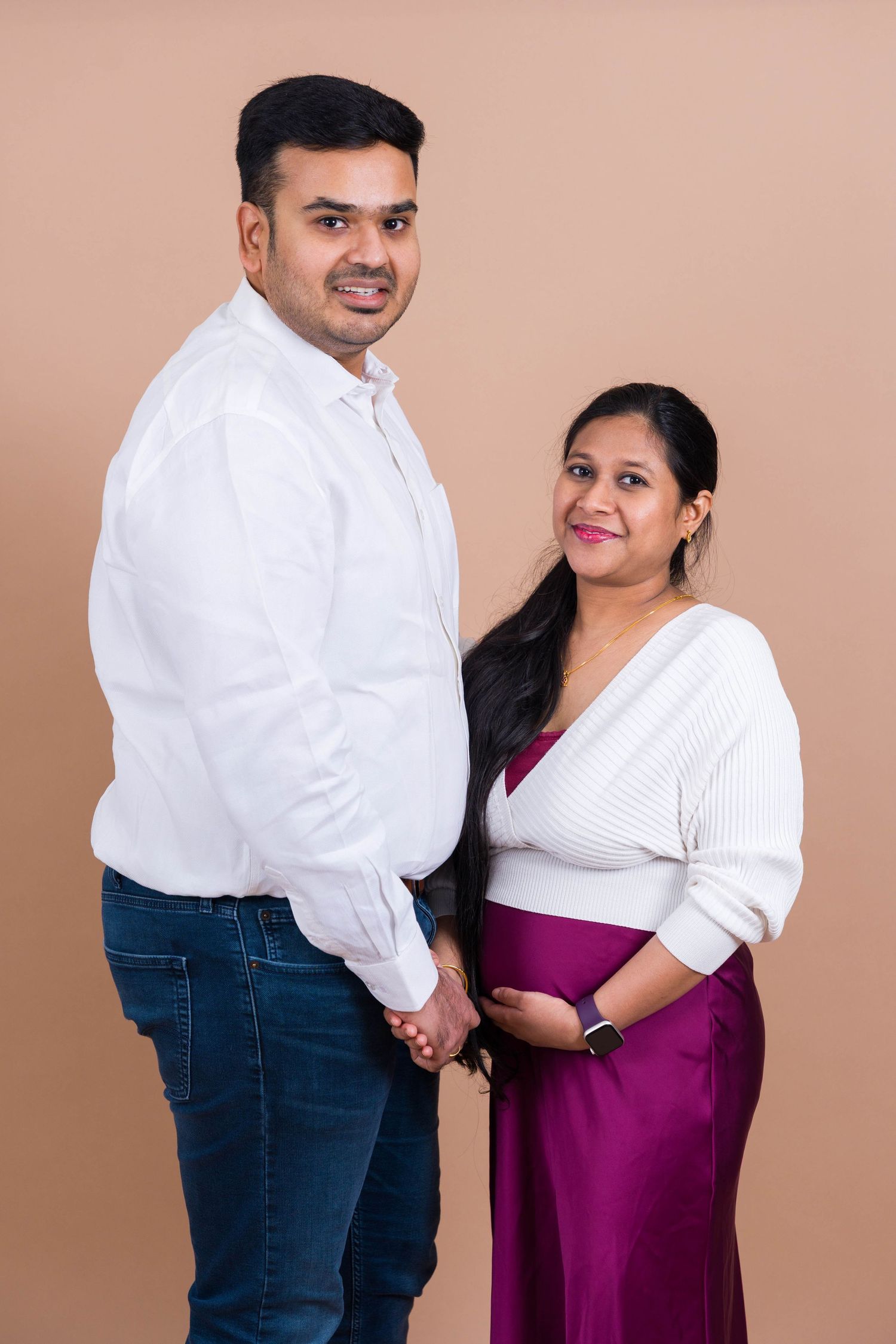 A couple in white and purple attire poses together against a brown backdrop for a formal portrait.